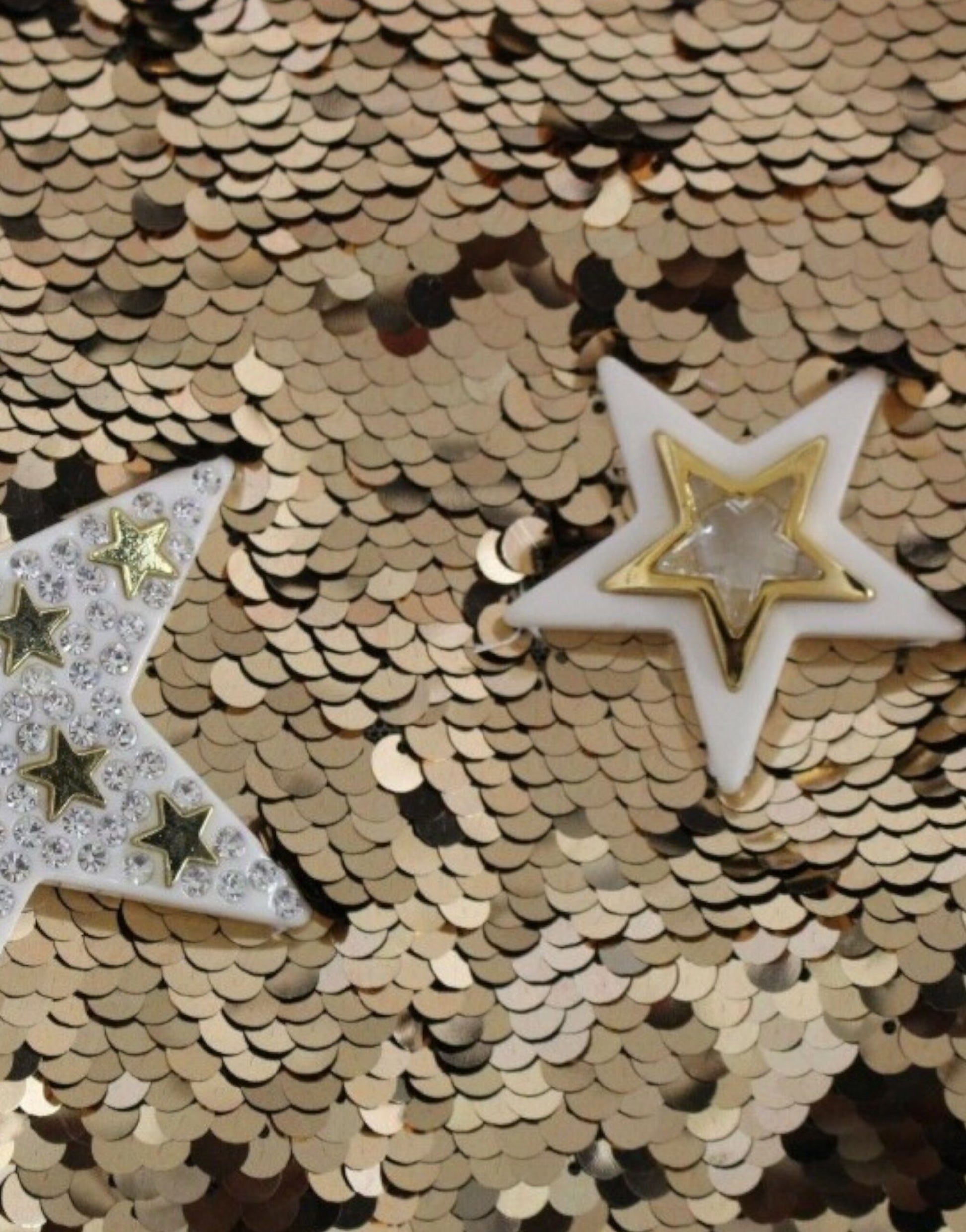 Two gold star shaped pins on a glittery background