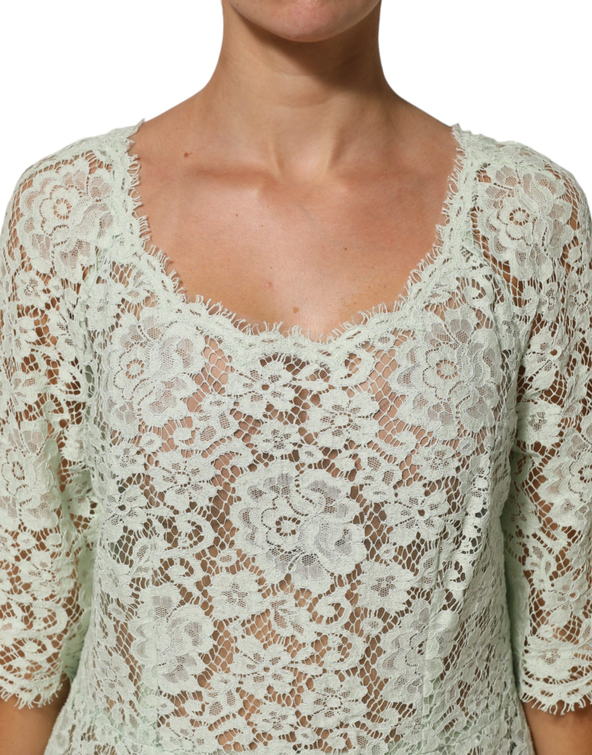 A woman wearing a mint green lace dress with floral trim and midi length