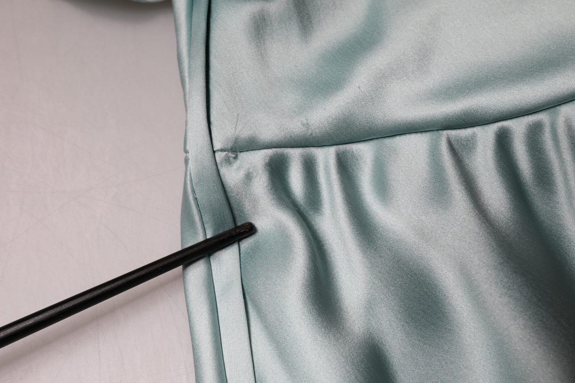 A close-up view of a fabric item with a shiny texture, possibly a dress or a skirt. There is a black object t