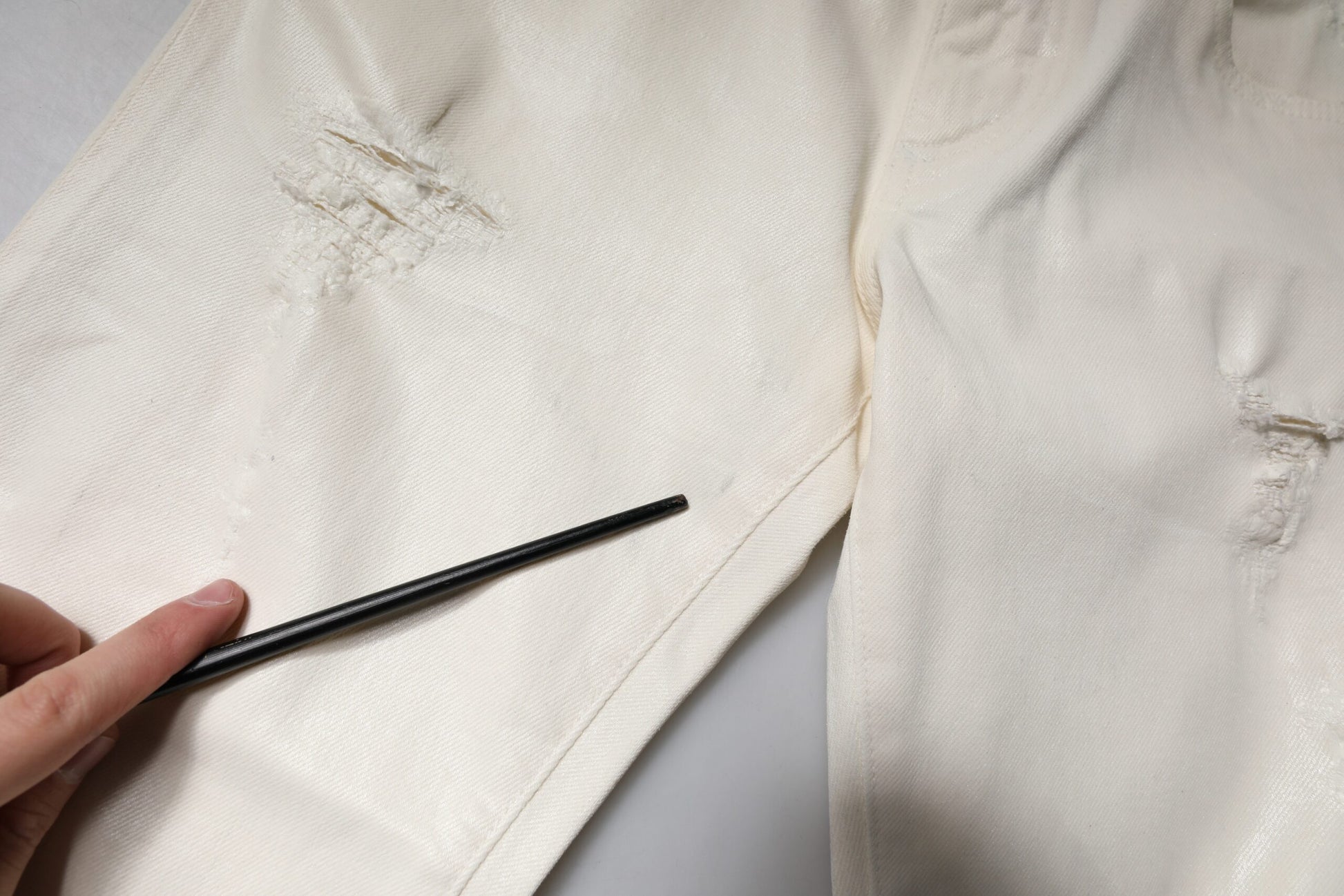 Hand holding black object over torn fabric