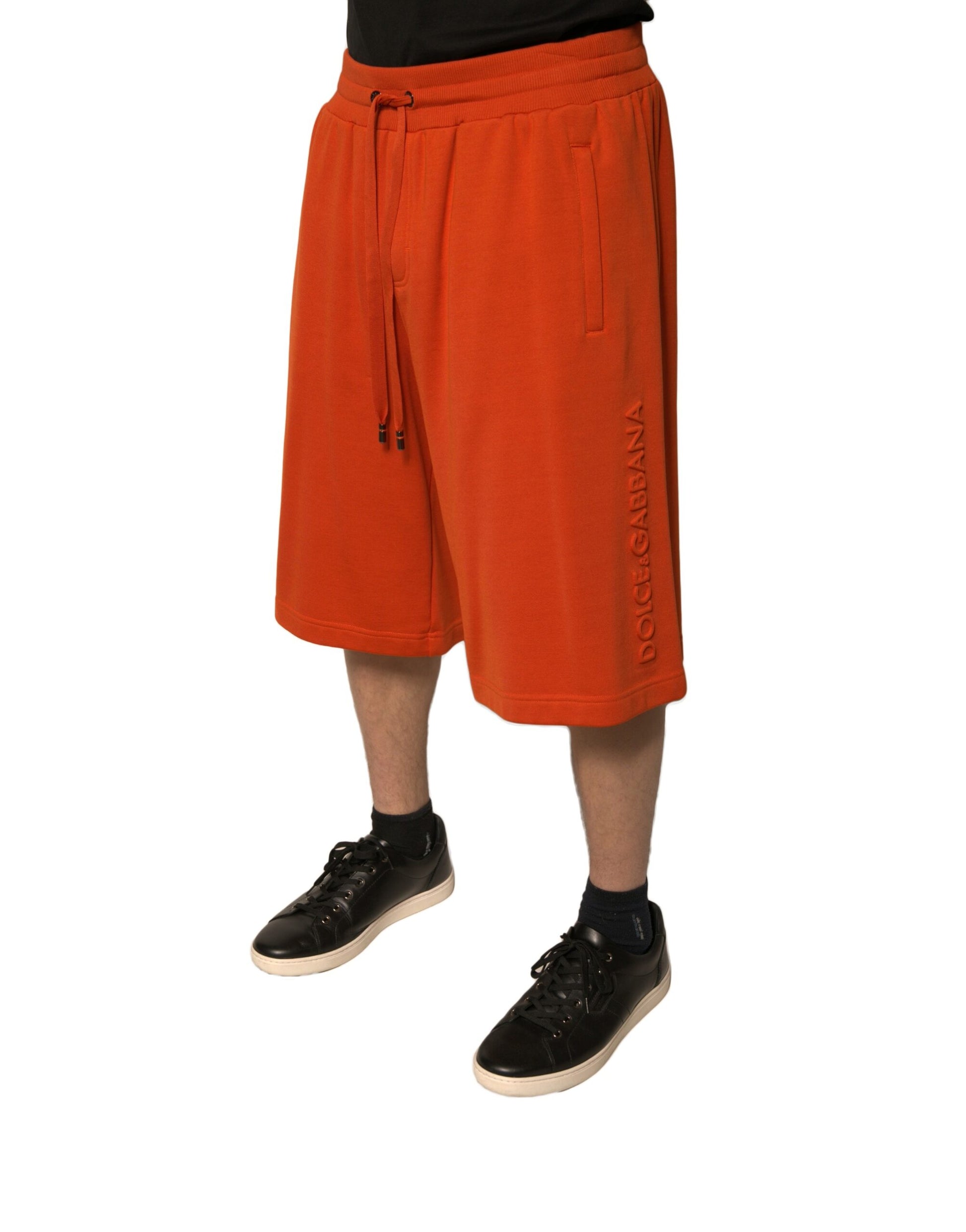 A pair of orange cotton blend men's bermuda shorts with a logo on the left leg
