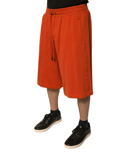 A pair of orange cotton blend men's bermuda shorts with a logo on the left leg