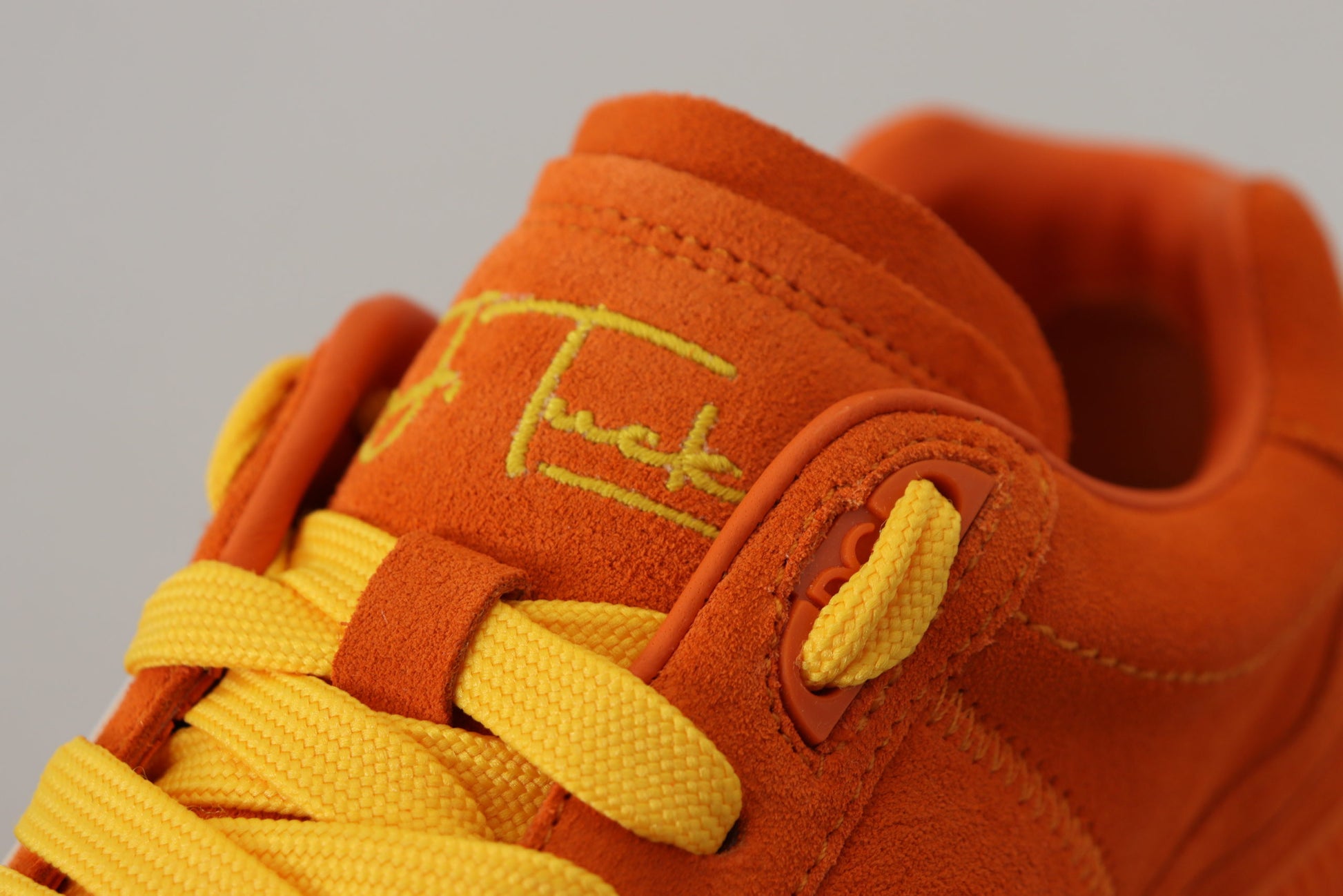 Orange baby shoe with yellow laces and a white logo on the side