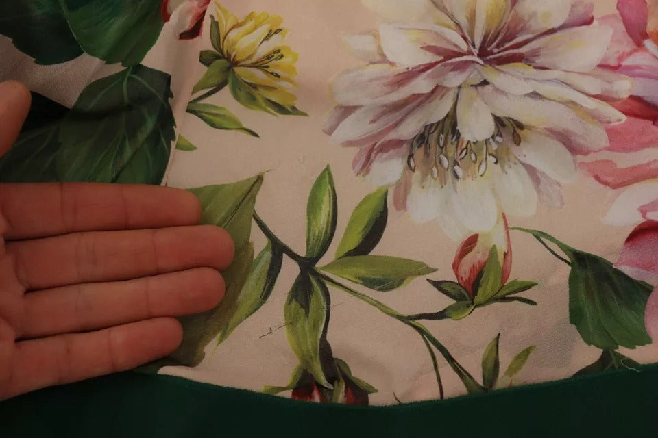 A person holding up a dress with floral patterns and a pussy bow detail