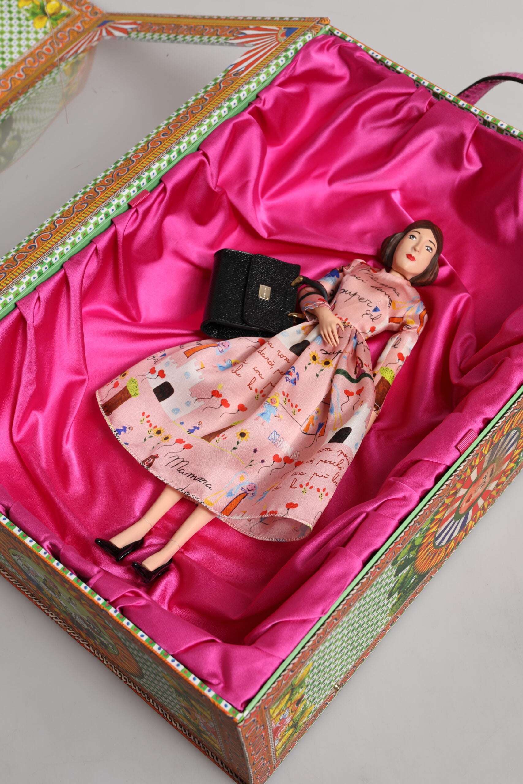 A porcelain doll wearing a pink dress with floral print, leather details and black heels