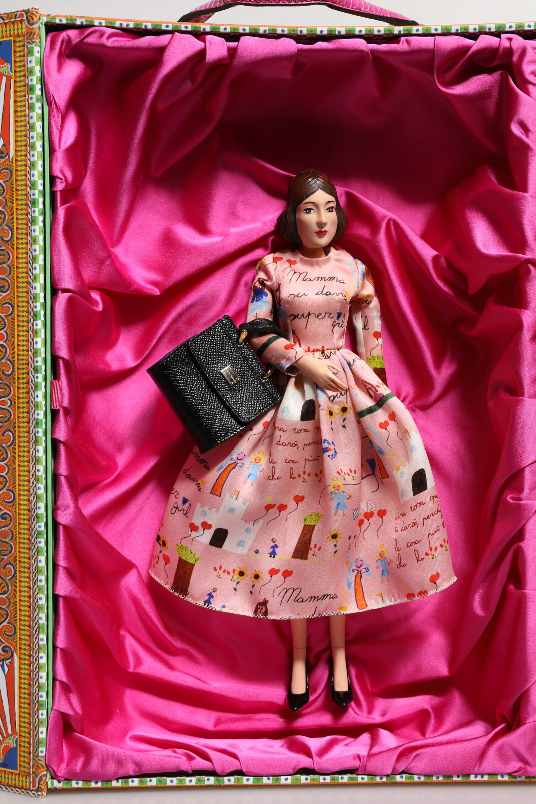 A porcelain doll wearing a pink dress with floral patterns, holding a black purse