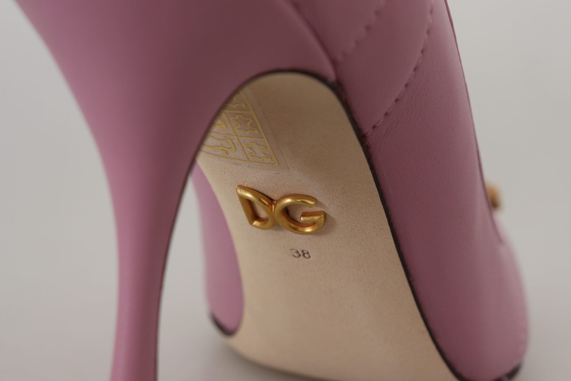 Pink high heel shoe with gold accents and a logo on the side
