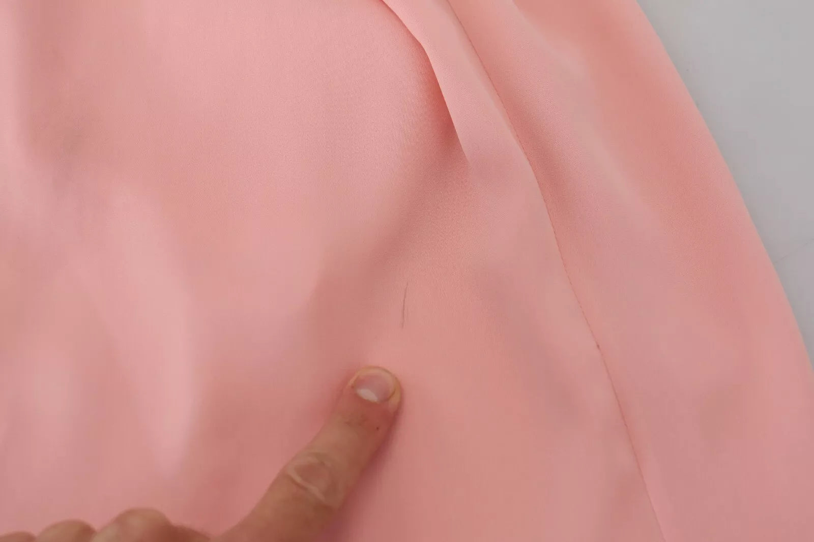 A person's hand pointing at a pink silk stretch strapless sheath midi dress