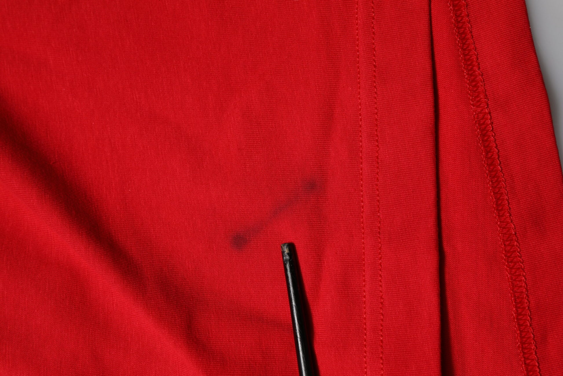 Red fabric with black stitching and a small hole
