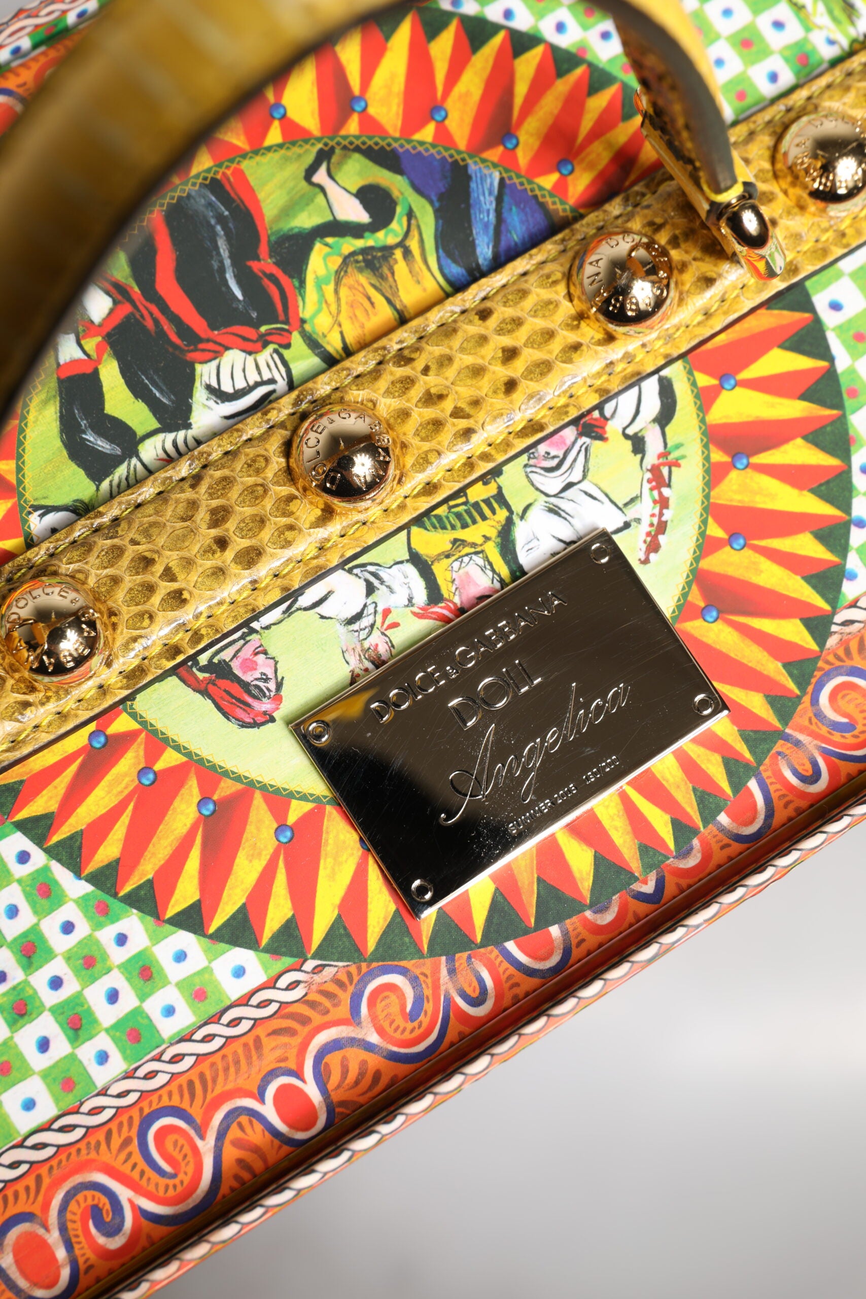 A colorful ceramic box with a leather handle, featuring a red dress and dolls