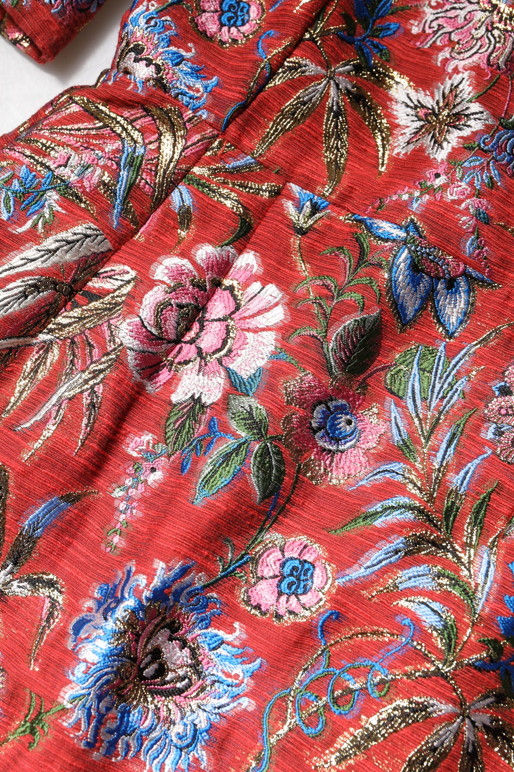 A red floral jacquard dress with an A-line silhouette. It features a detailed embroidery pattern and is desig