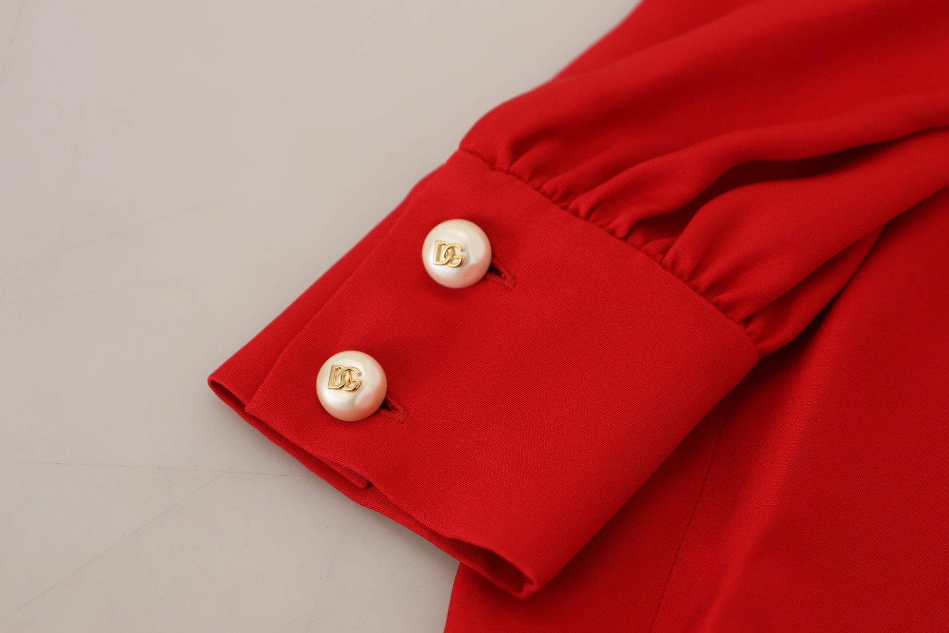 A red silk sheath dress with a knee length and an A-line cut. It features pearl buttons on the sleeve cuffs