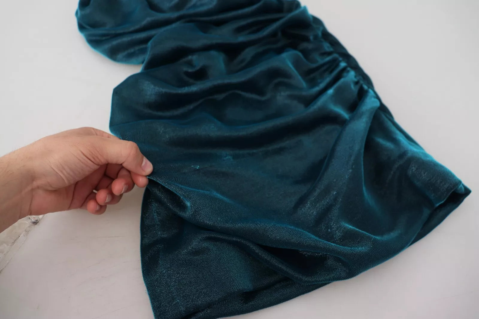 A person's hand holding a blue satin fitted strapless dress with a silky blend fabric