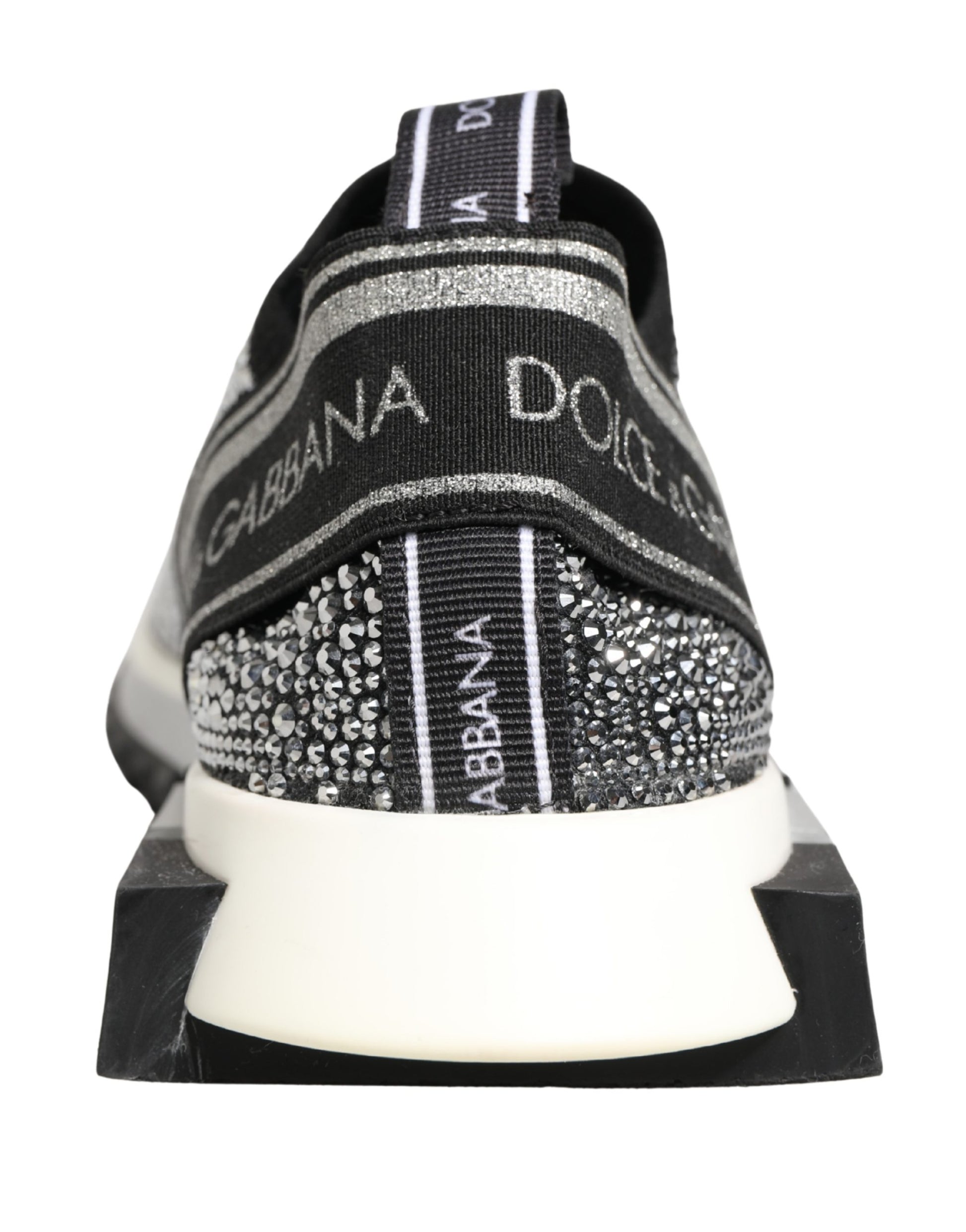 A pair of silver slip-on shoes with a crystal logo on the side