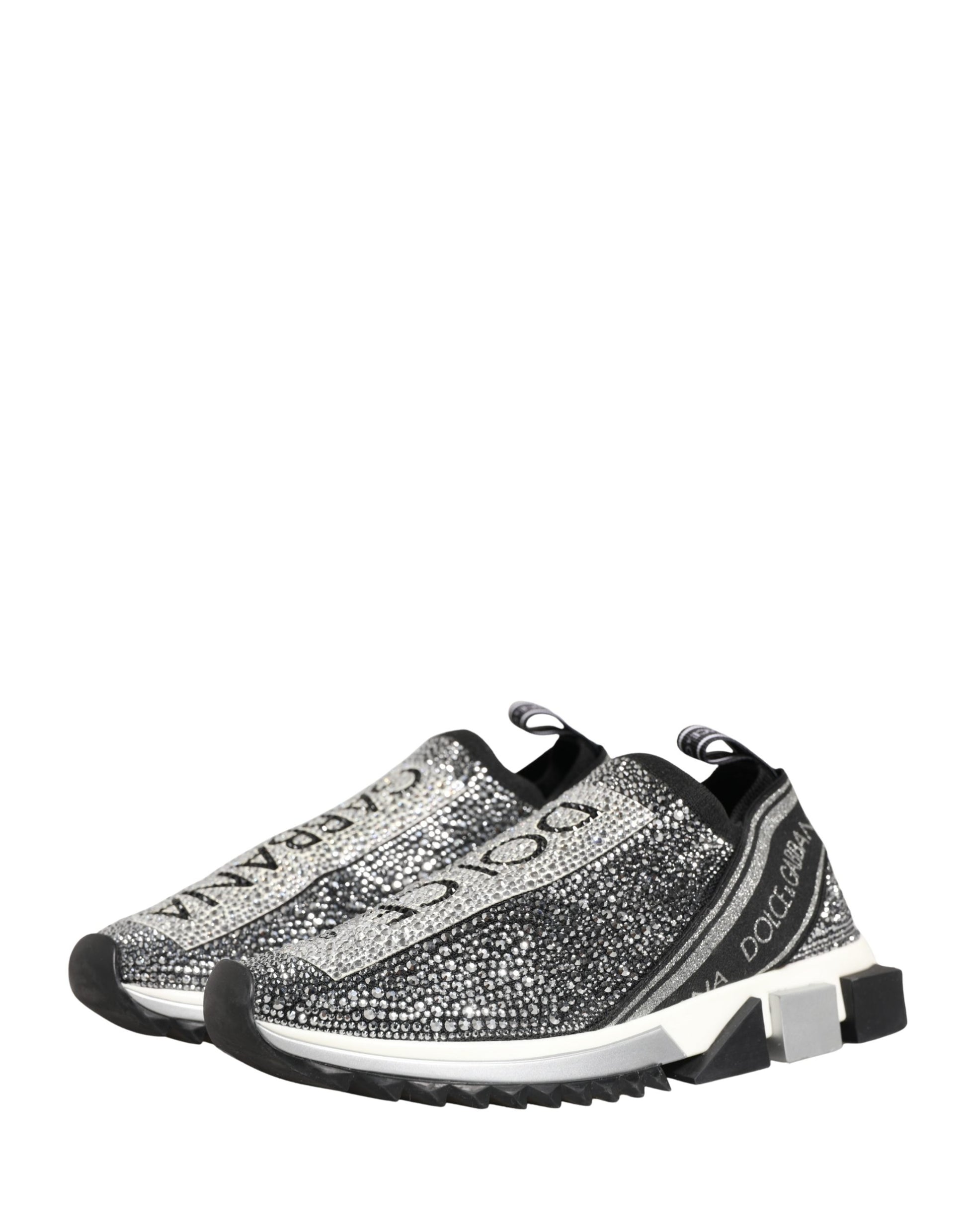 A pair of silver slip-on shoes with a crystal logo on the side