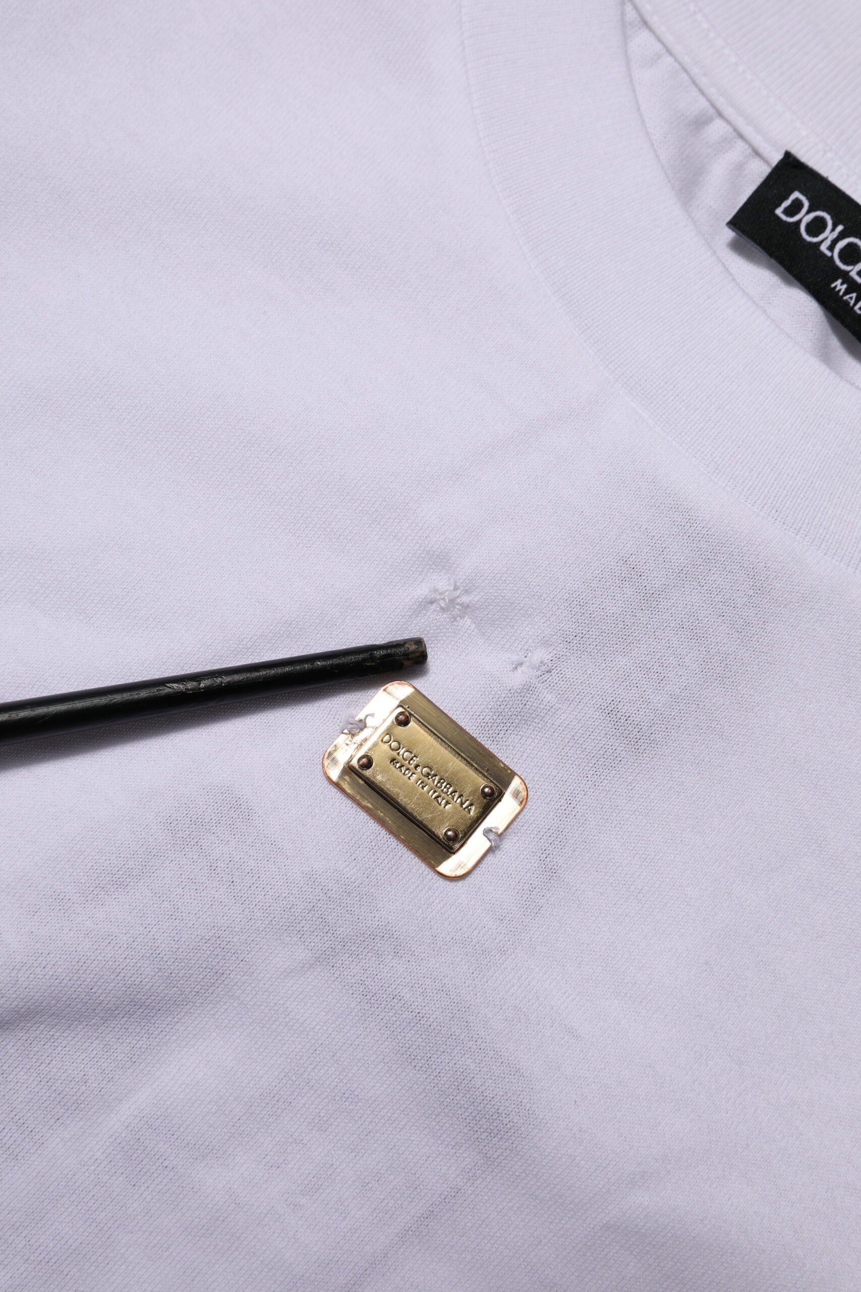 White t-shirt with a small gold pin on it
