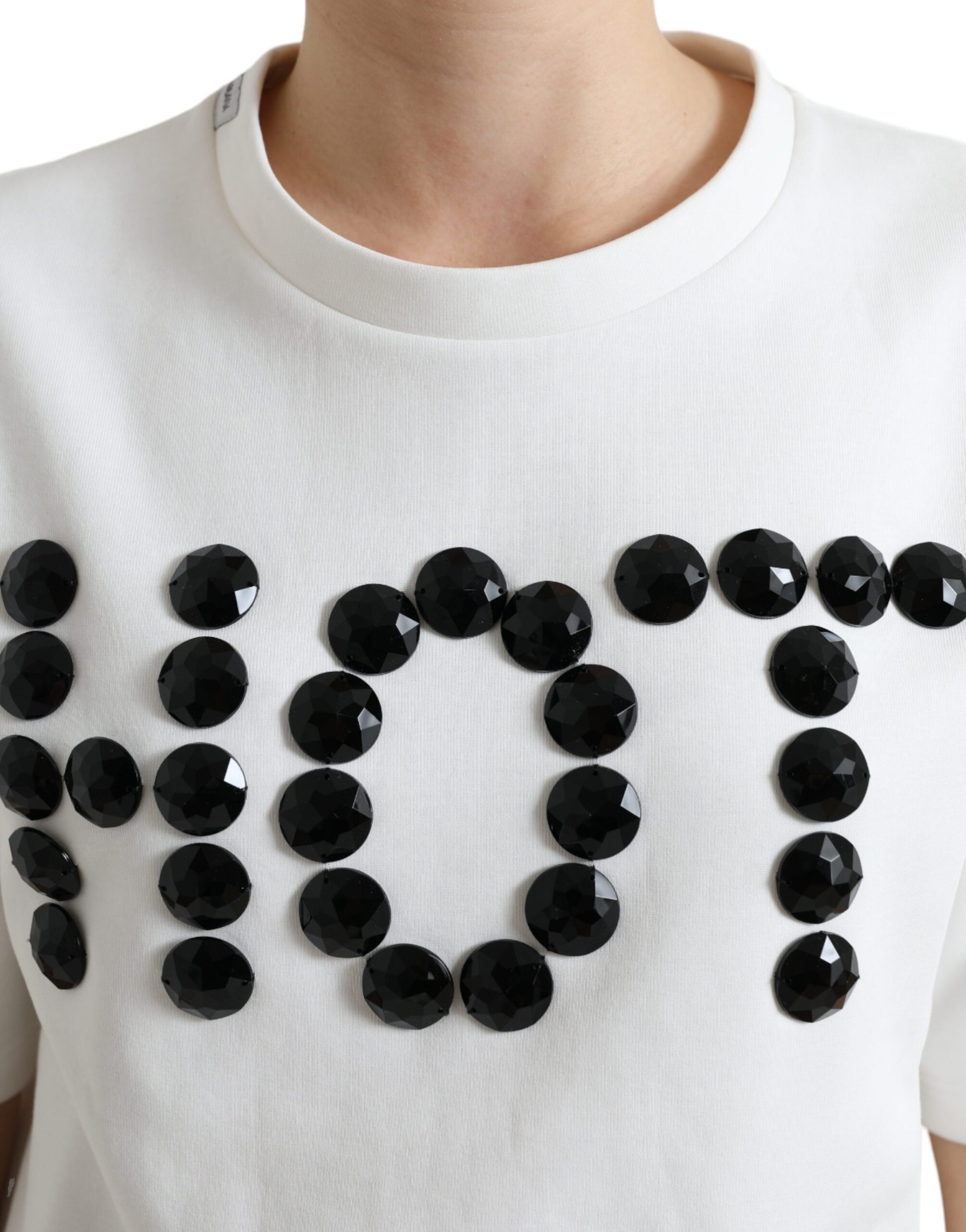 White sweater with black letters spelling "NOT" made from sequins or similar embellishments