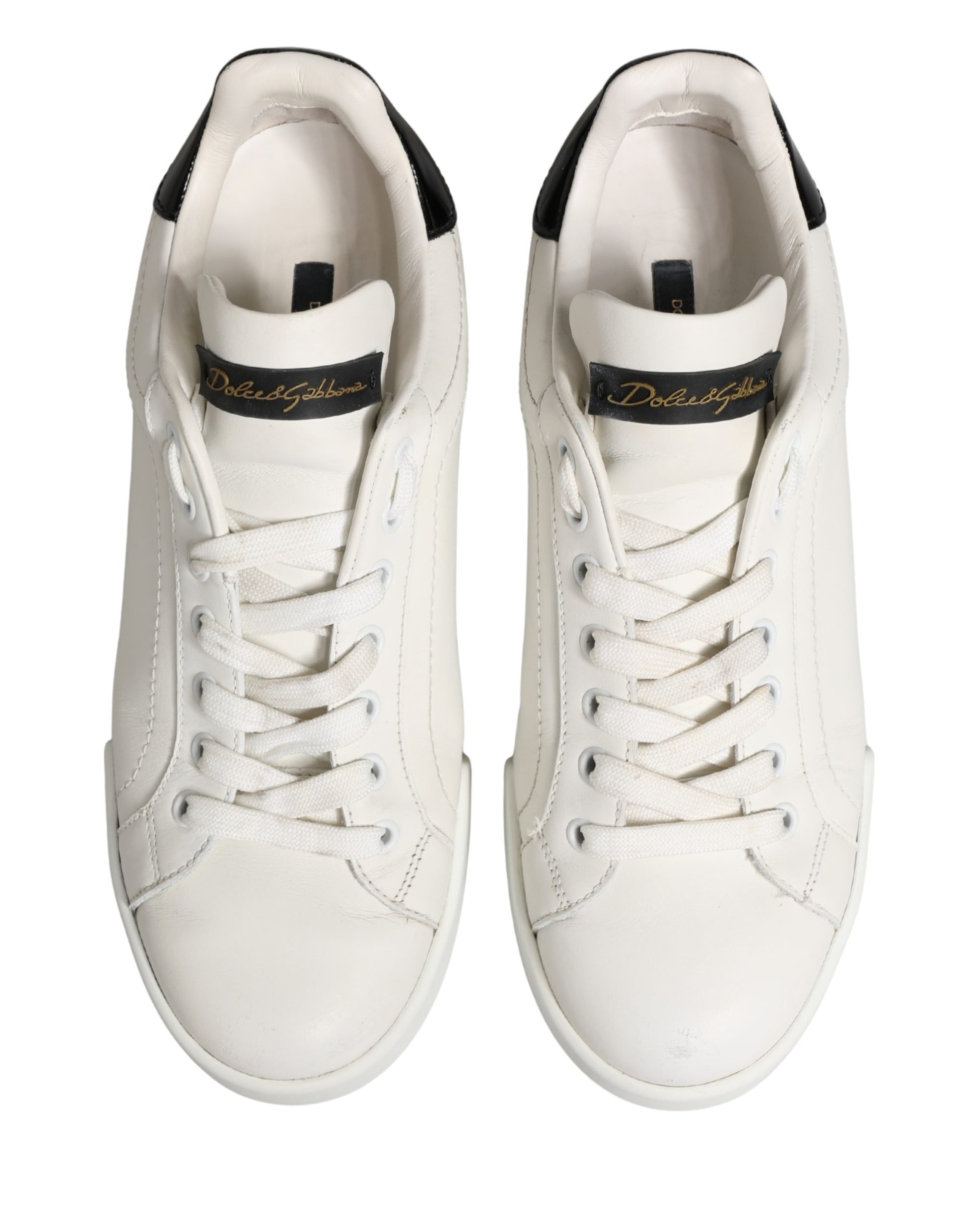 Pair of white leather sneakers with black accents and gold branding, featuring a low-top design