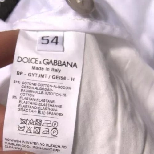 A pair of white chinos with a label indicating they are made by Dolce & Gabbana, made in Italy. The tag also includes care in