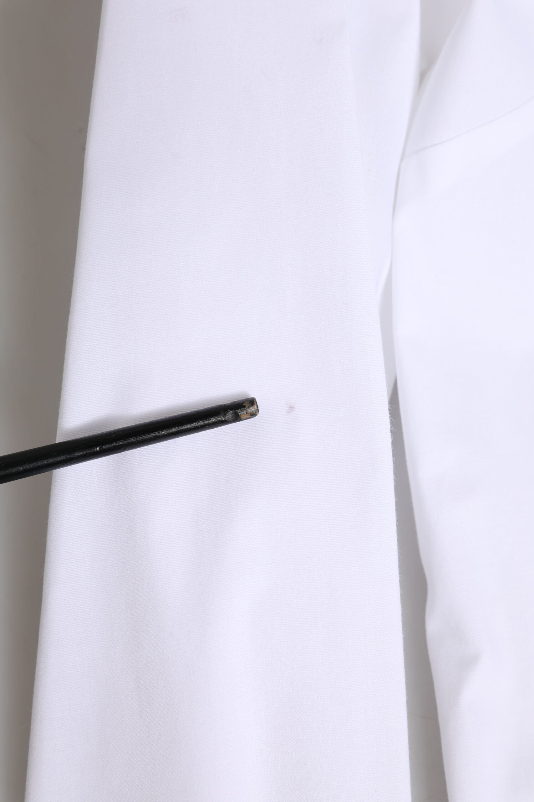 A white cotton collared buttoned dress shirt top with a black tie pin