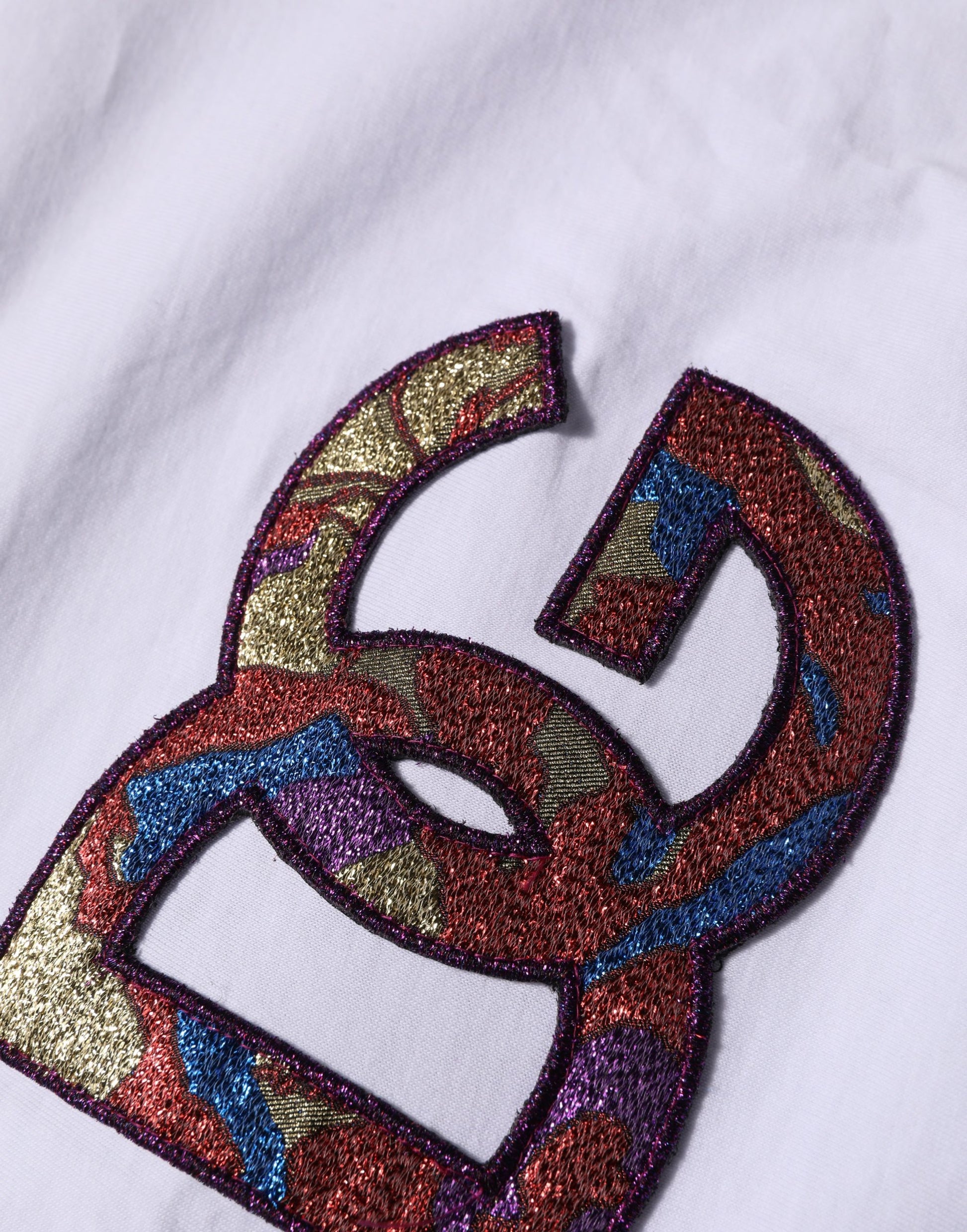 A white crew neck t-shirt with a colorful embroidered logo patch