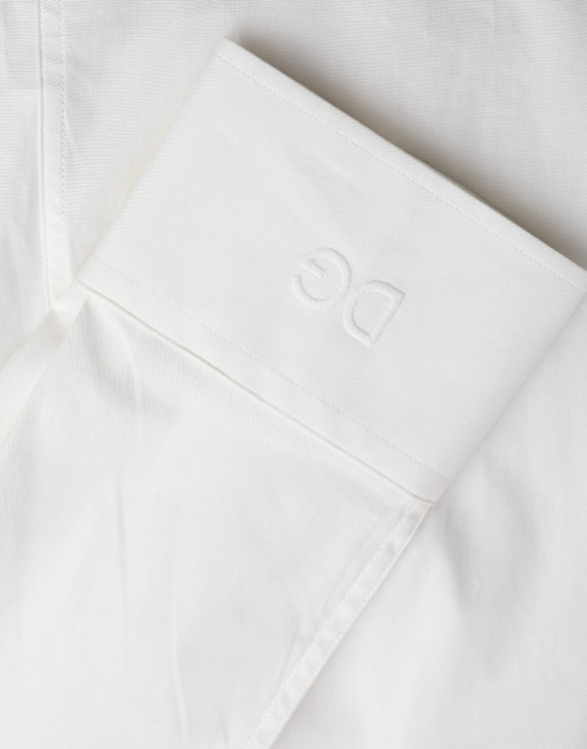 A white cotton dress with a slim fit and gold shirt detailing