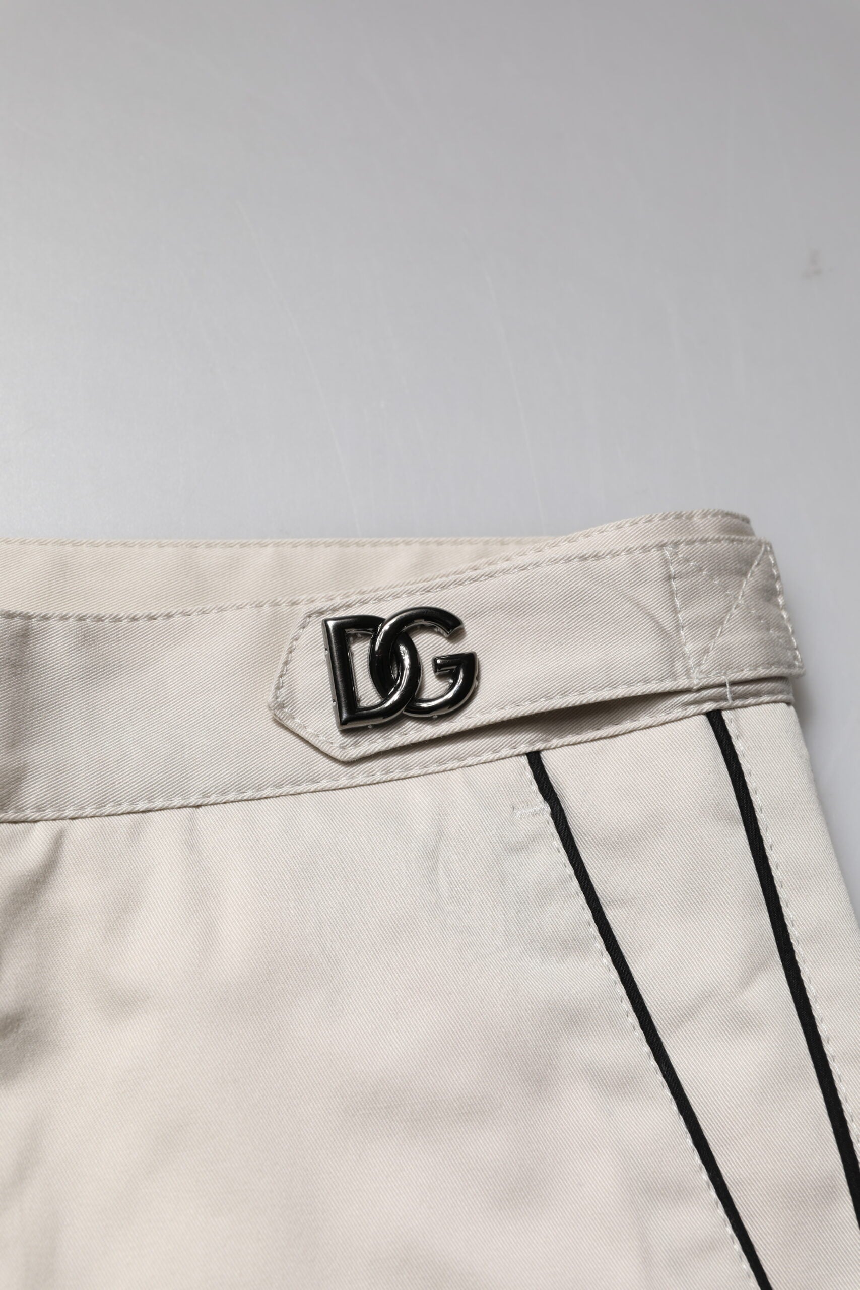 A pair of white cotton dress pants with a slim fit, featuring the Dolce & Gabbana logo on the waistband