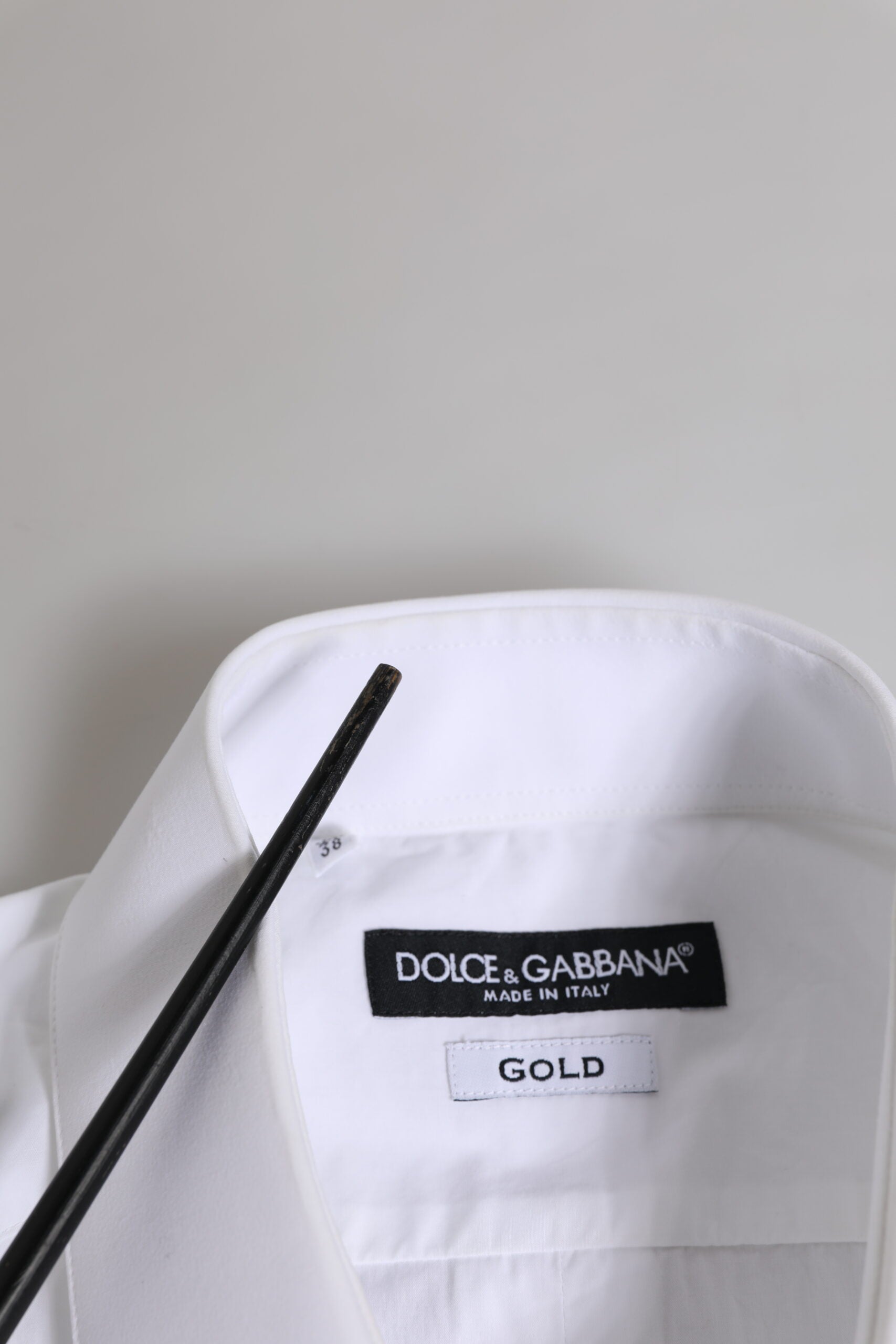 A white cotton shirt with long sleeves and a gold label on the front