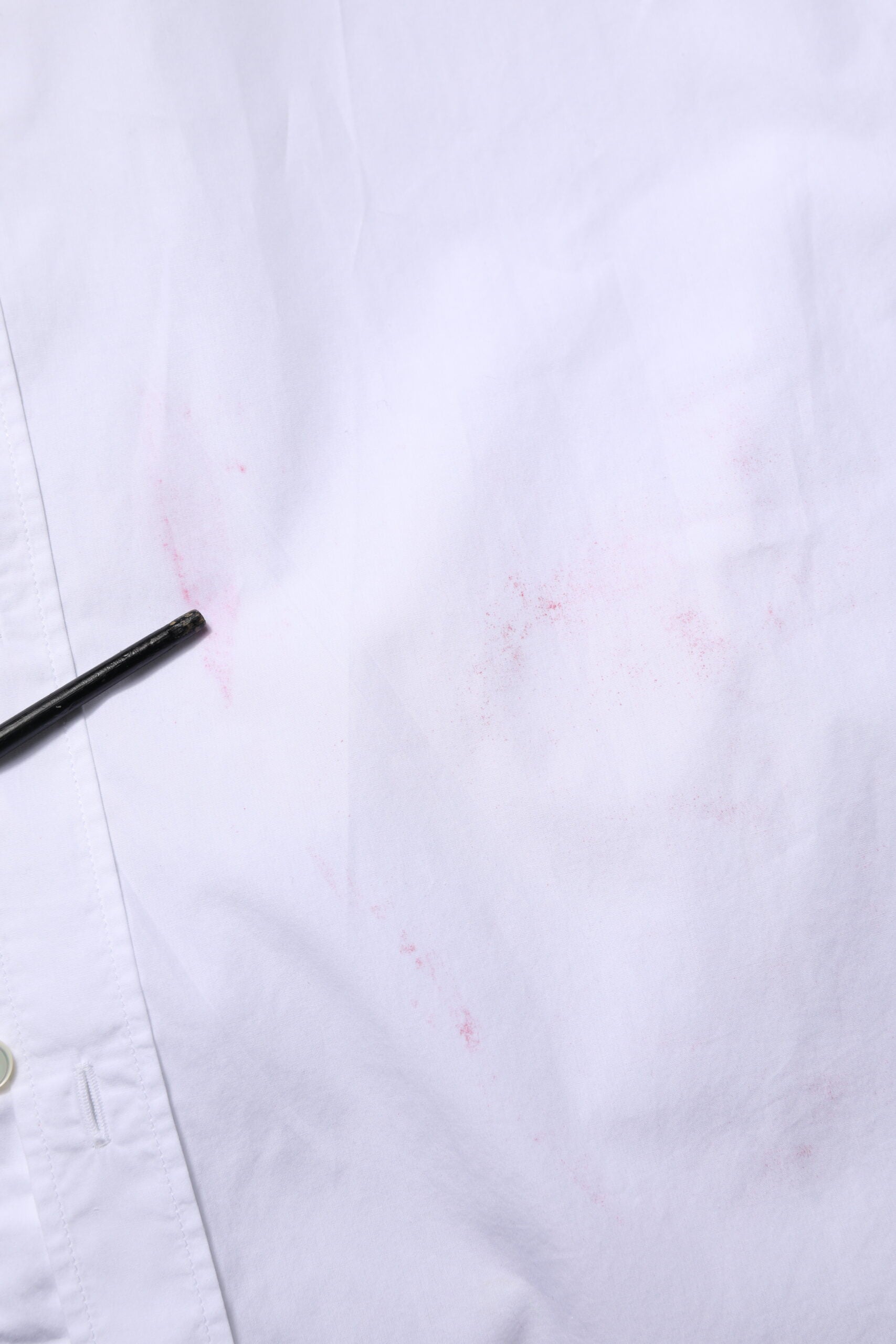 A white cotton long sleeve dress shirt with a pink stain on the front