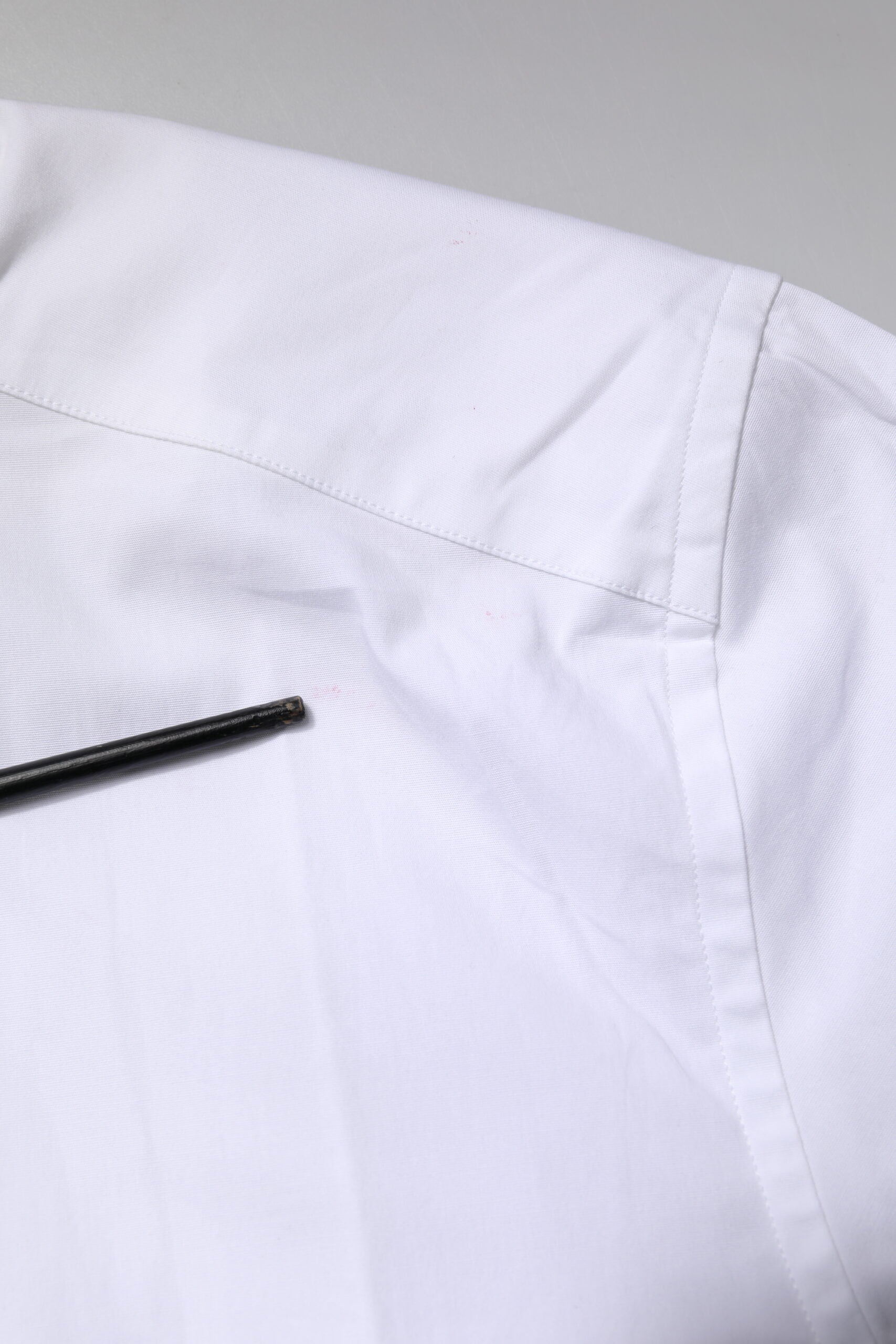 A white cotton stretch dress shirt with a gold pin on the left shoulder