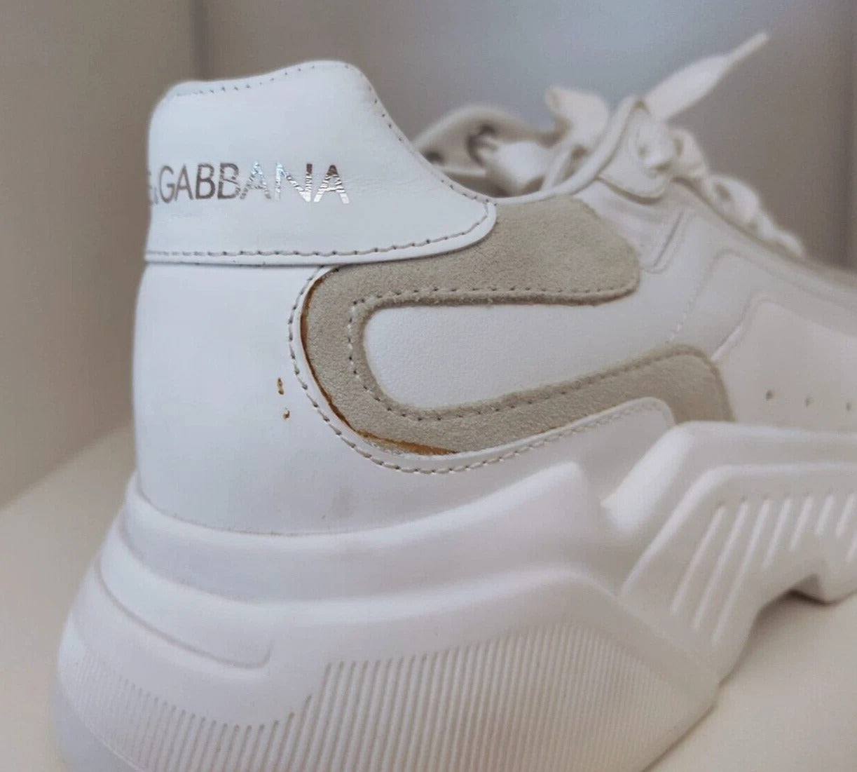 A pair of white sneakers with tan accents, featuring a logo on the side and a low top design