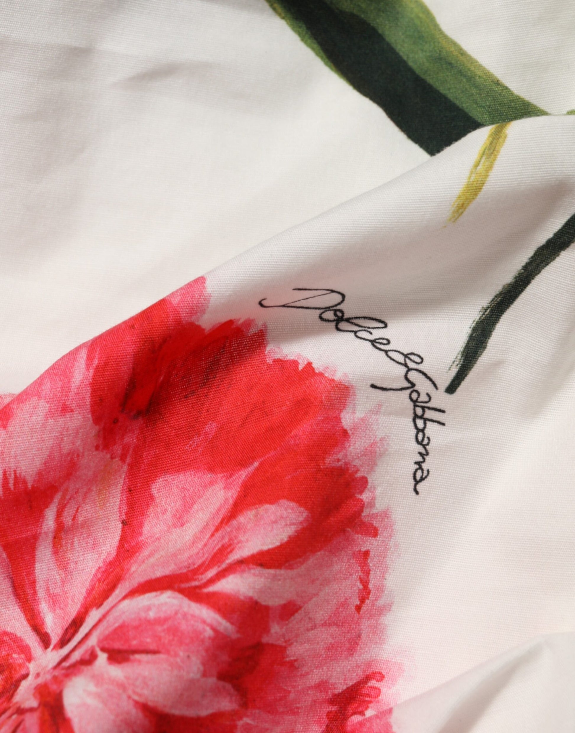 A white floral one shoulder sheath dress with red flowers and a signature on the waistband