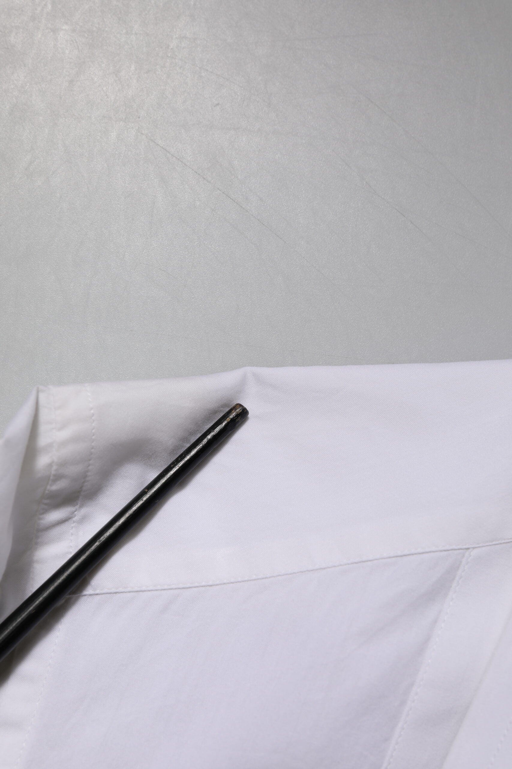 A black pen resting on a white cotton poplin dress shirt with gold accents