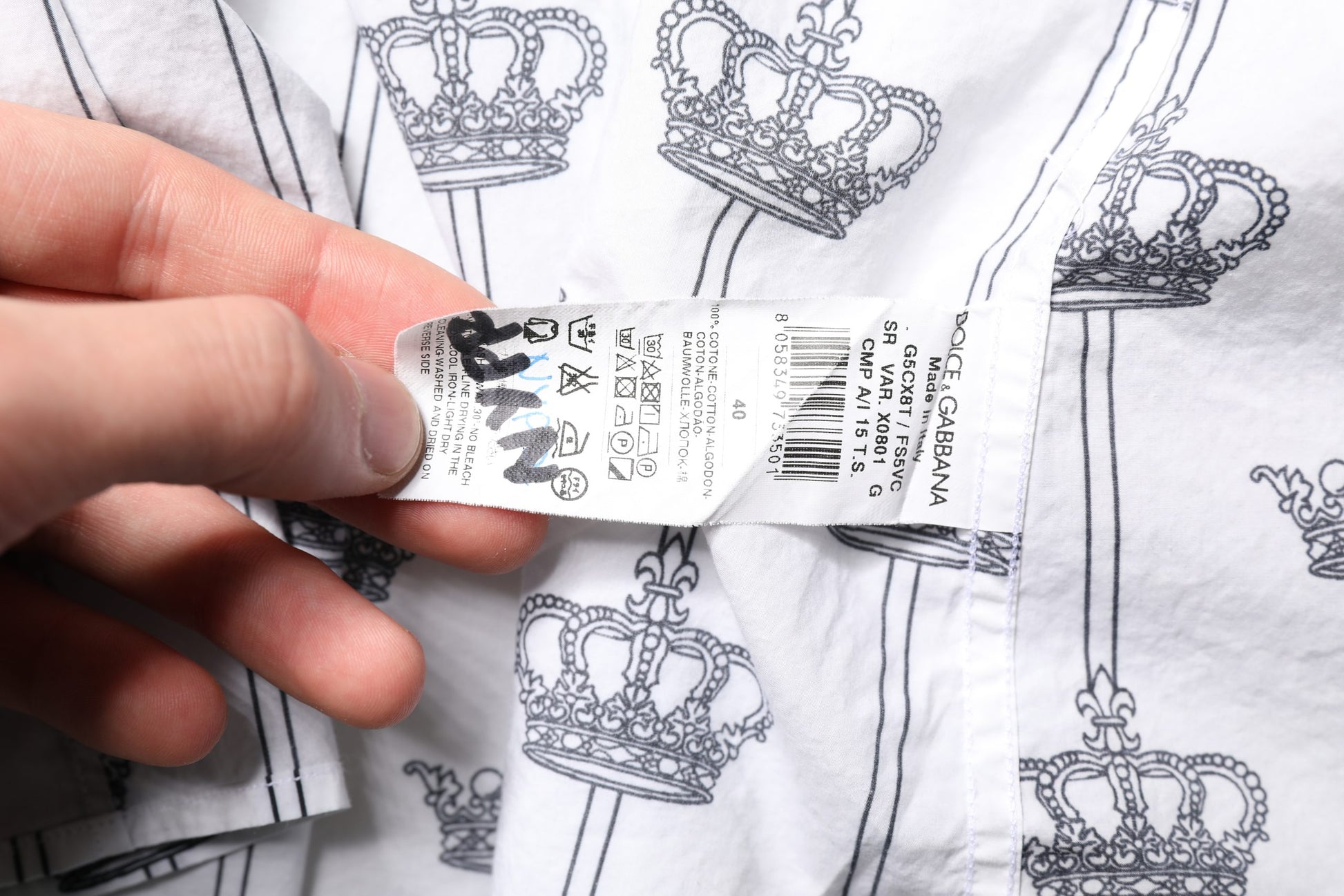 A person's hand holding a white dress with gold crown pattern, part of a formal shirt