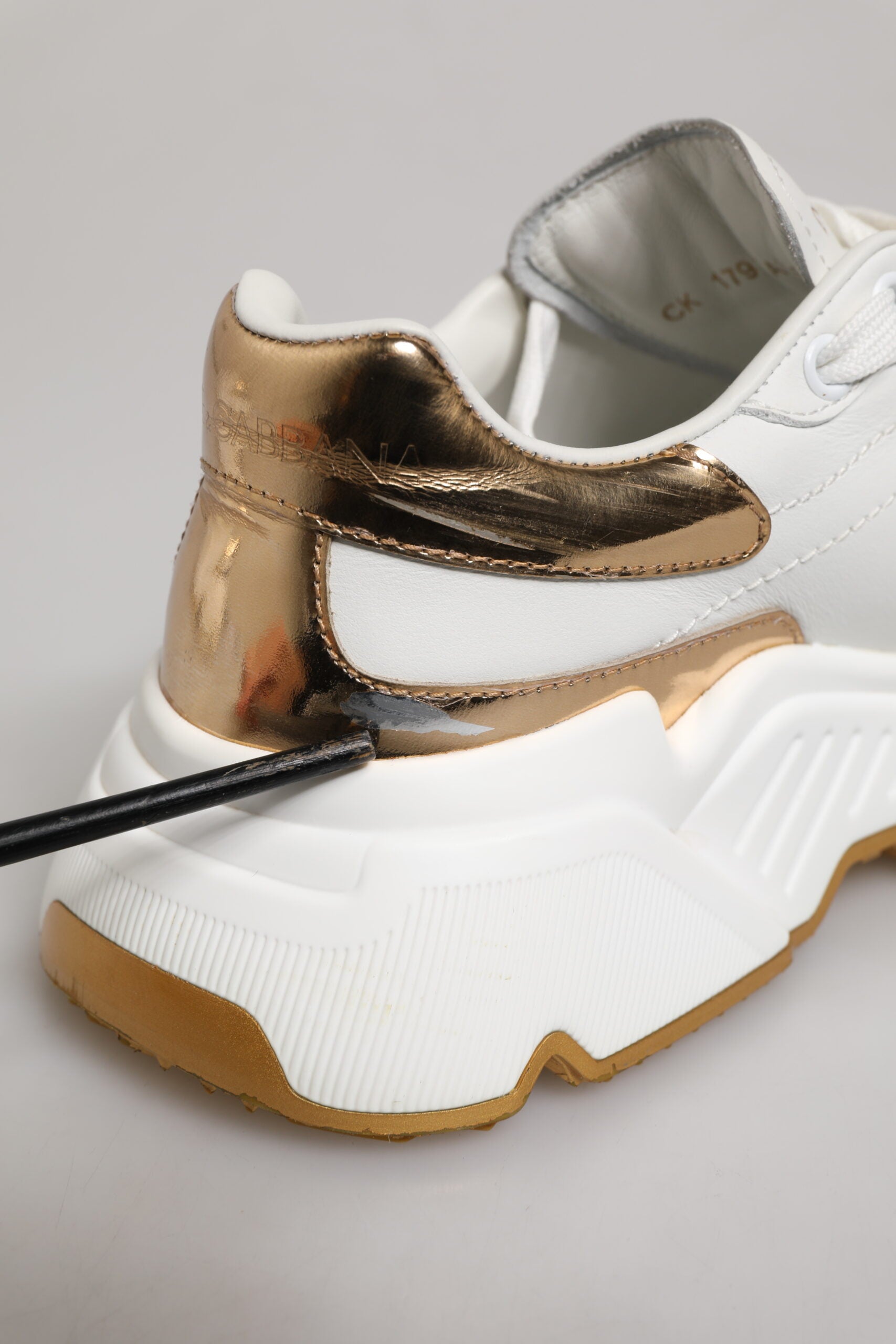 A pair of white gold leather sneakers with a black sole