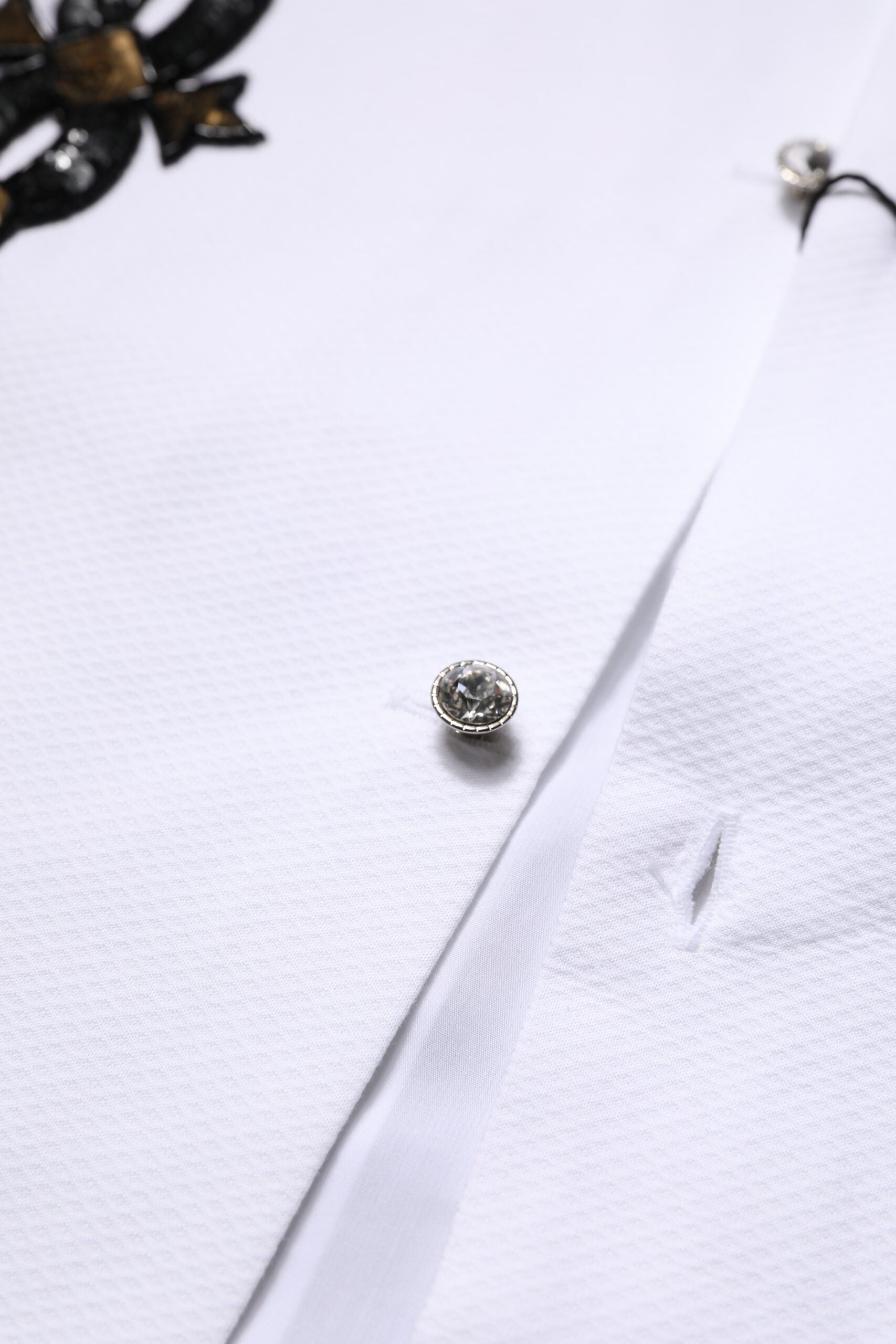 A white dress shirt with gold embellishments and a single button closure