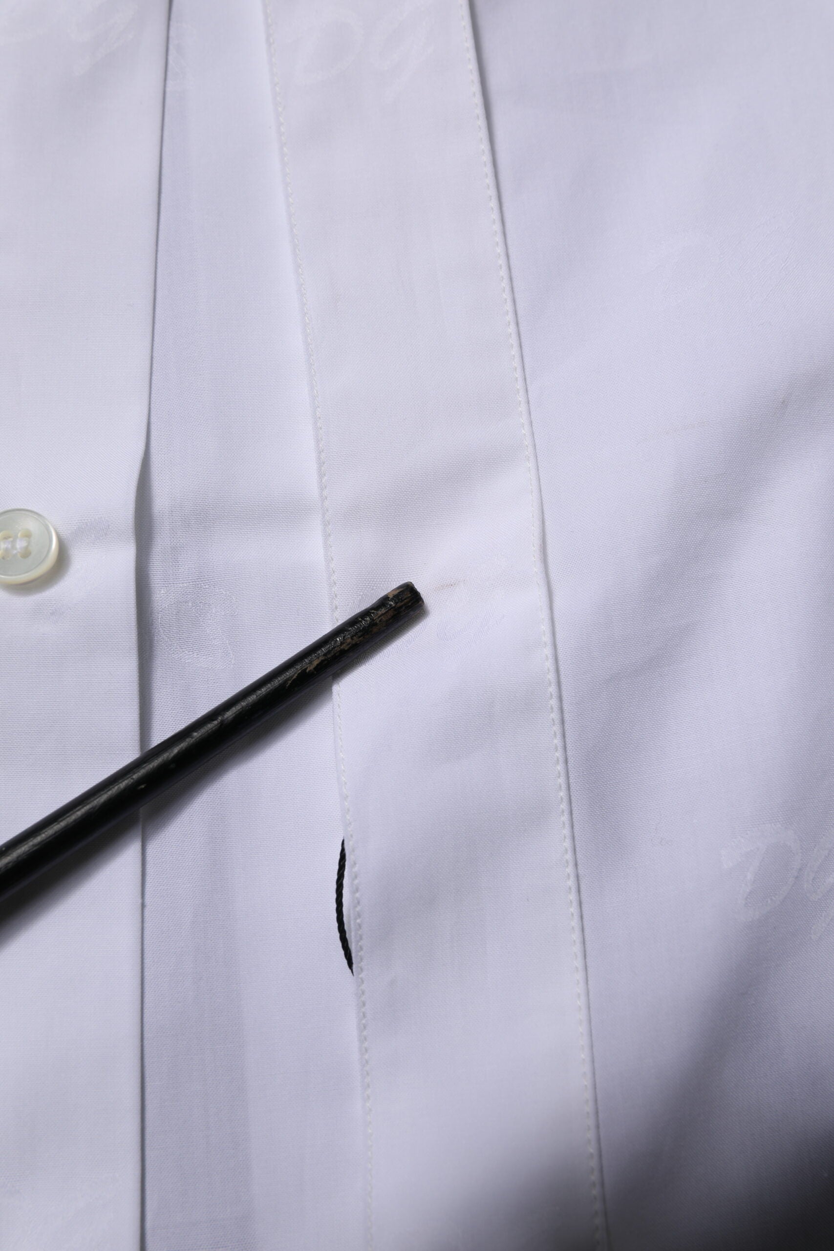 A white dress shirt with long sleeves and gold accents, featuring a button-up front