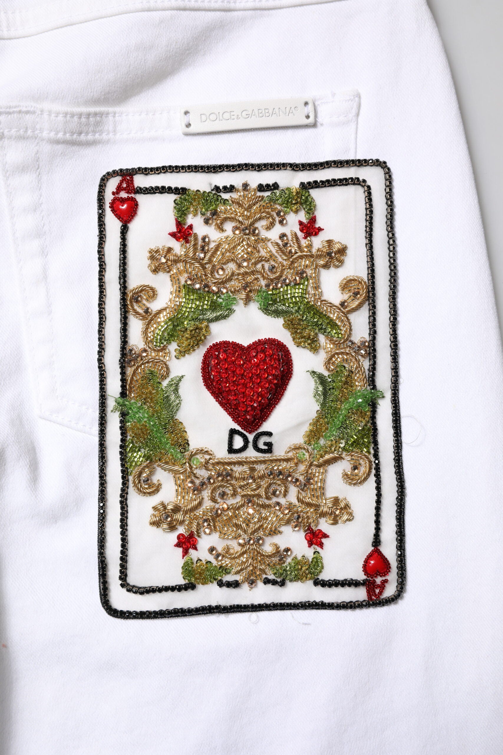 White jeans with embroidered playing card featuring a heart in the center