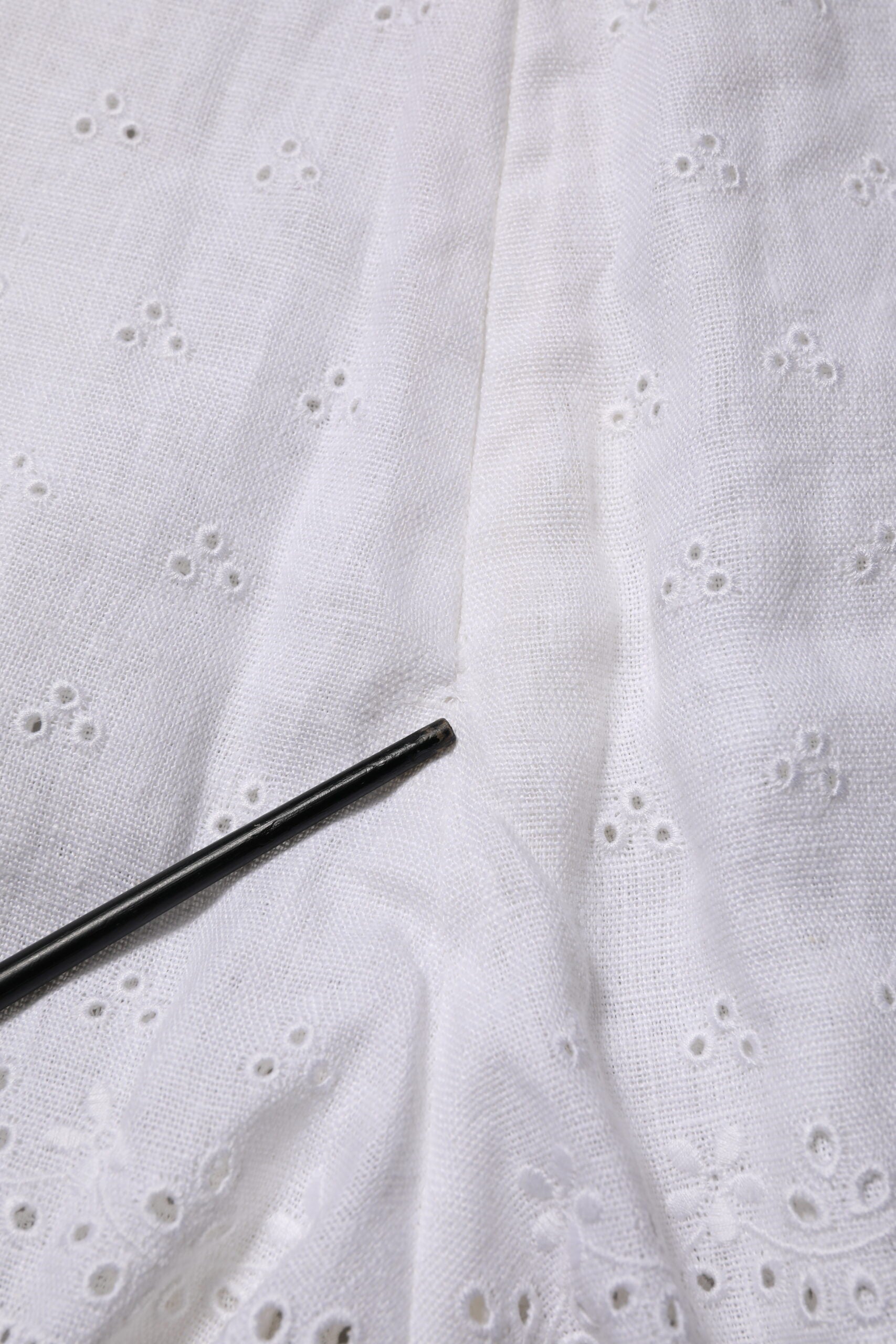 White fabric with holes, black needle for sewing