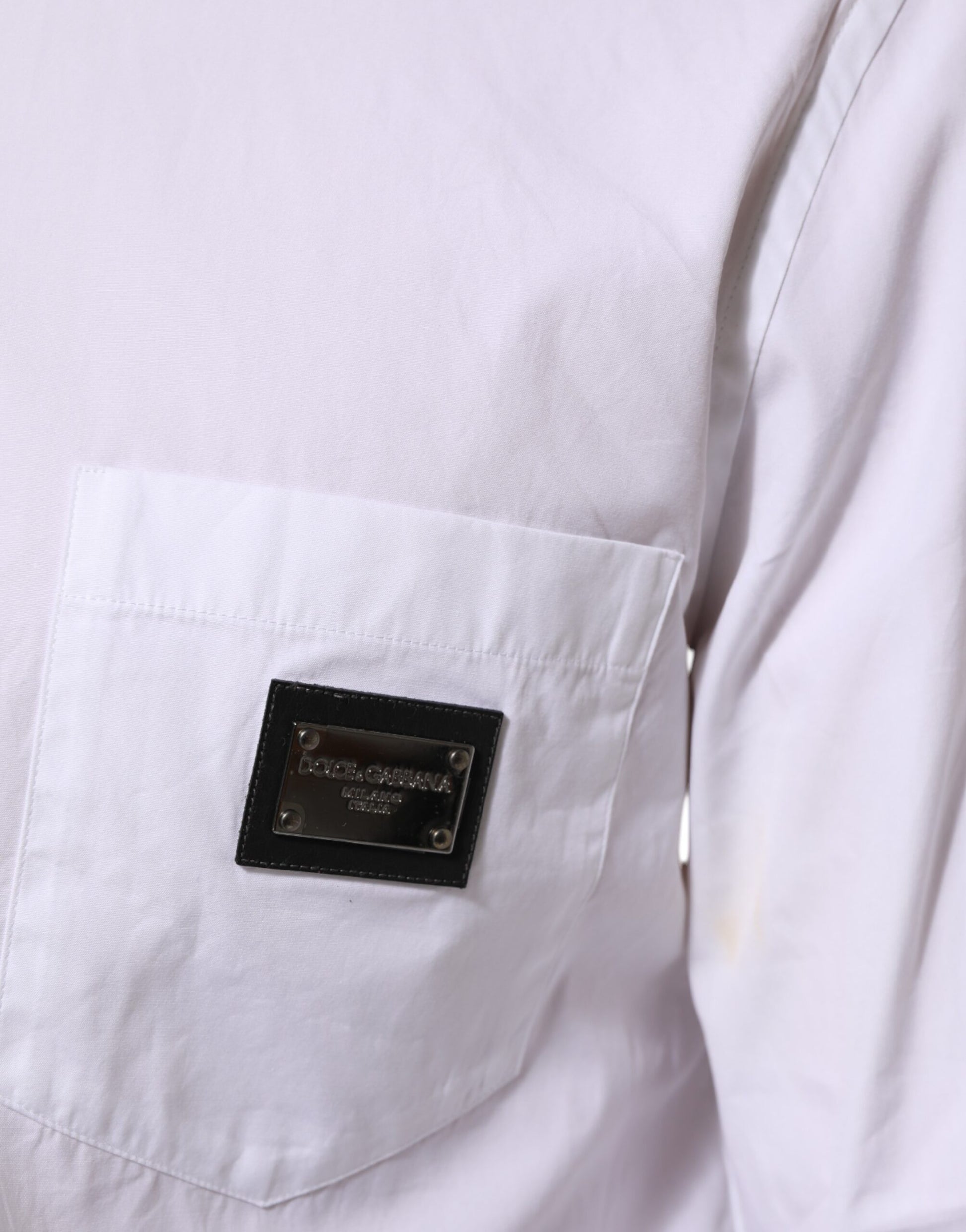 A white collared dress shirt with a black logo plaque on the left chest