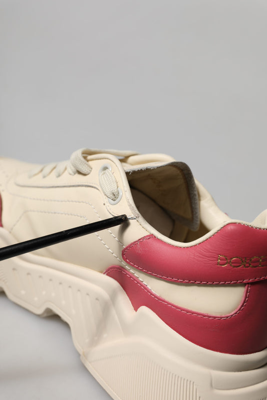 A pair of white pink leather sneakers with red accents, featuring a black Nike swoosh logo