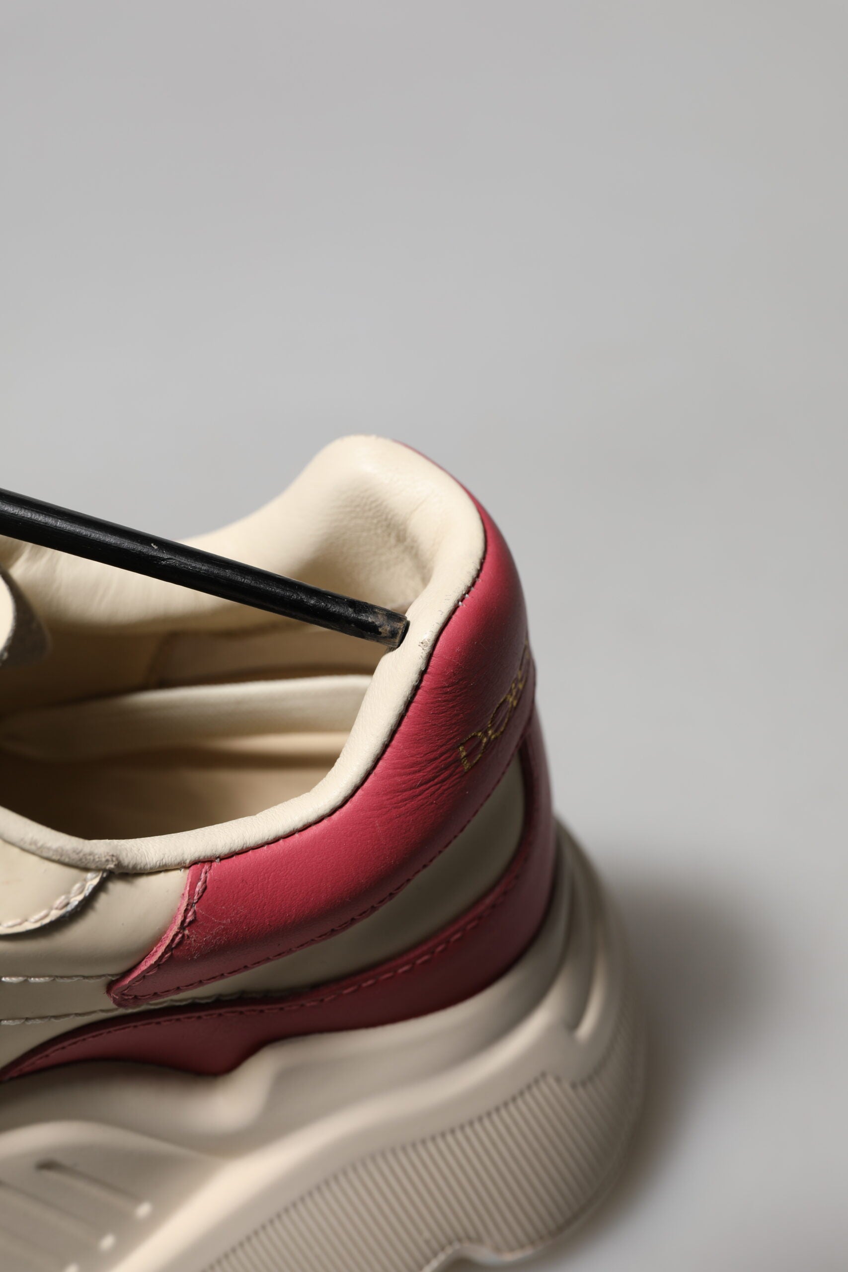 A pair of white pink leather sneakers with black laces and a red logo on the side