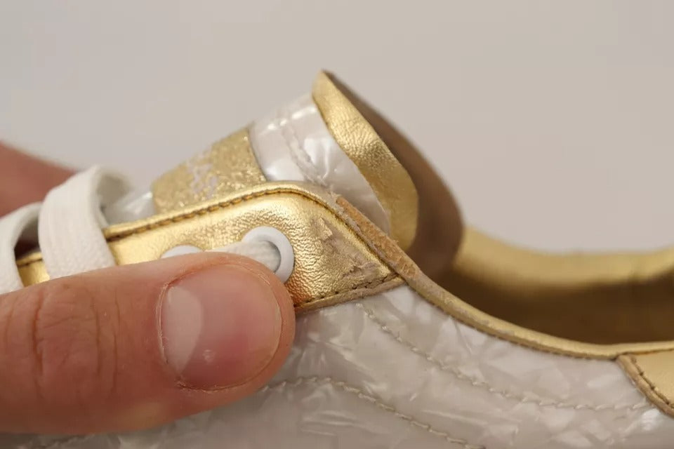 Hand holding white sneaker with gold accents, laces, and mother of pearl details