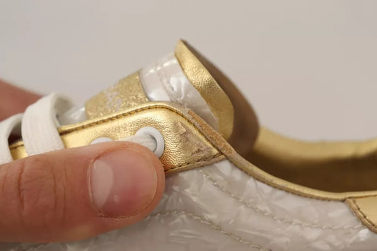 Hand holding white sneaker with gold accents, laces, and mother of pearl details