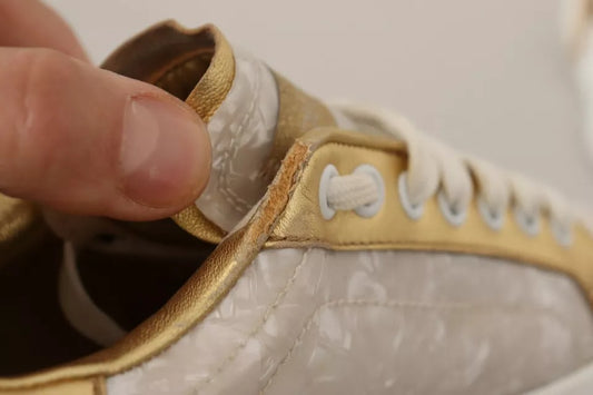 Hand holding open white sneaker with gold accents and mother of pearl details