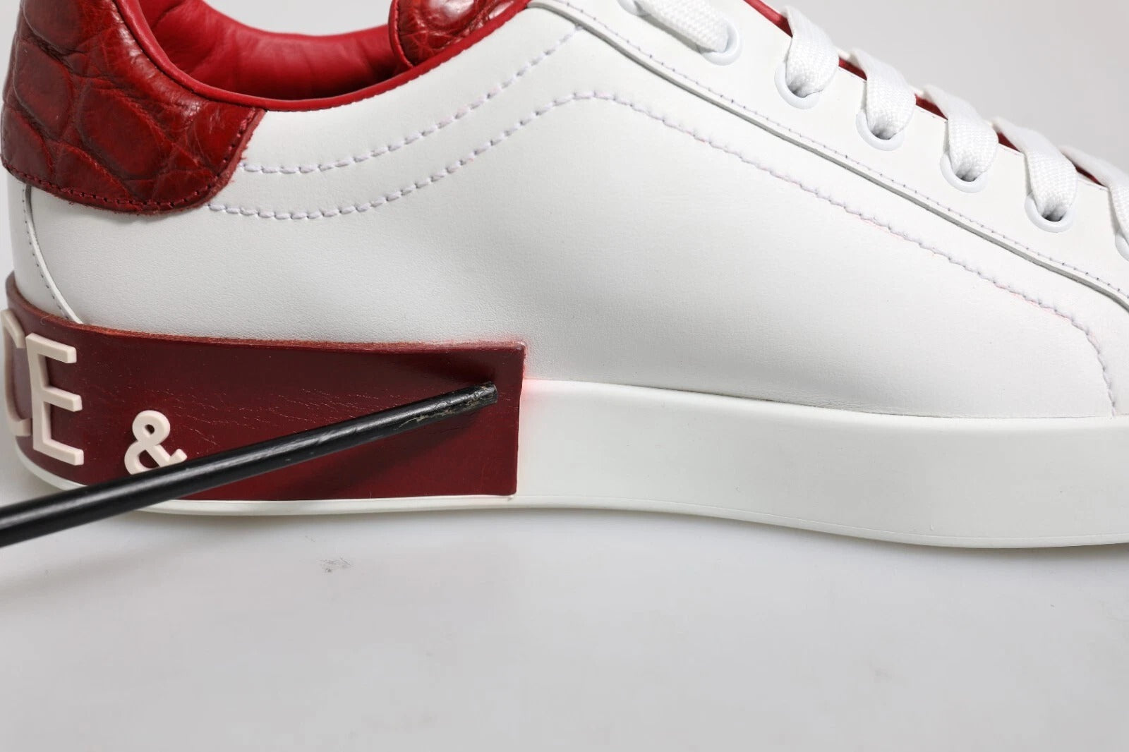 A white red leather sneaker with a logo on the side and a strap across the top