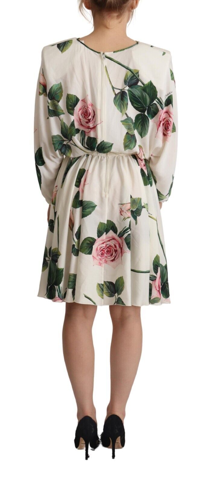 A woman wearing a white dress with a floral print featuring pink roses. The dress has long sleeves and is des