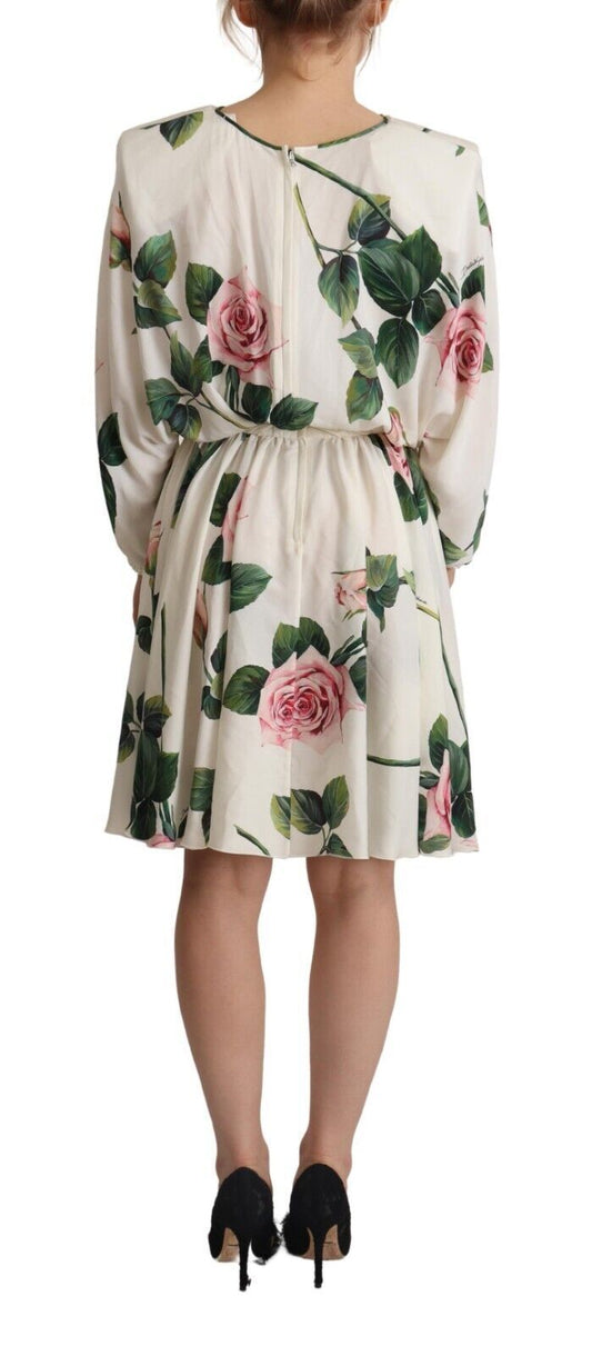 A woman wearing a white dress with a floral print featuring pink roses. The dress has long sleeves and is des