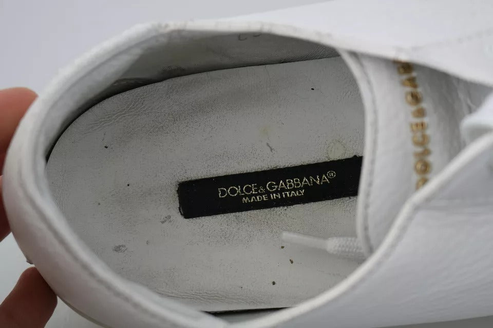 A white lace-up sneaker with a gold label on the tongue, indicating it's from Dolce & Gabbana