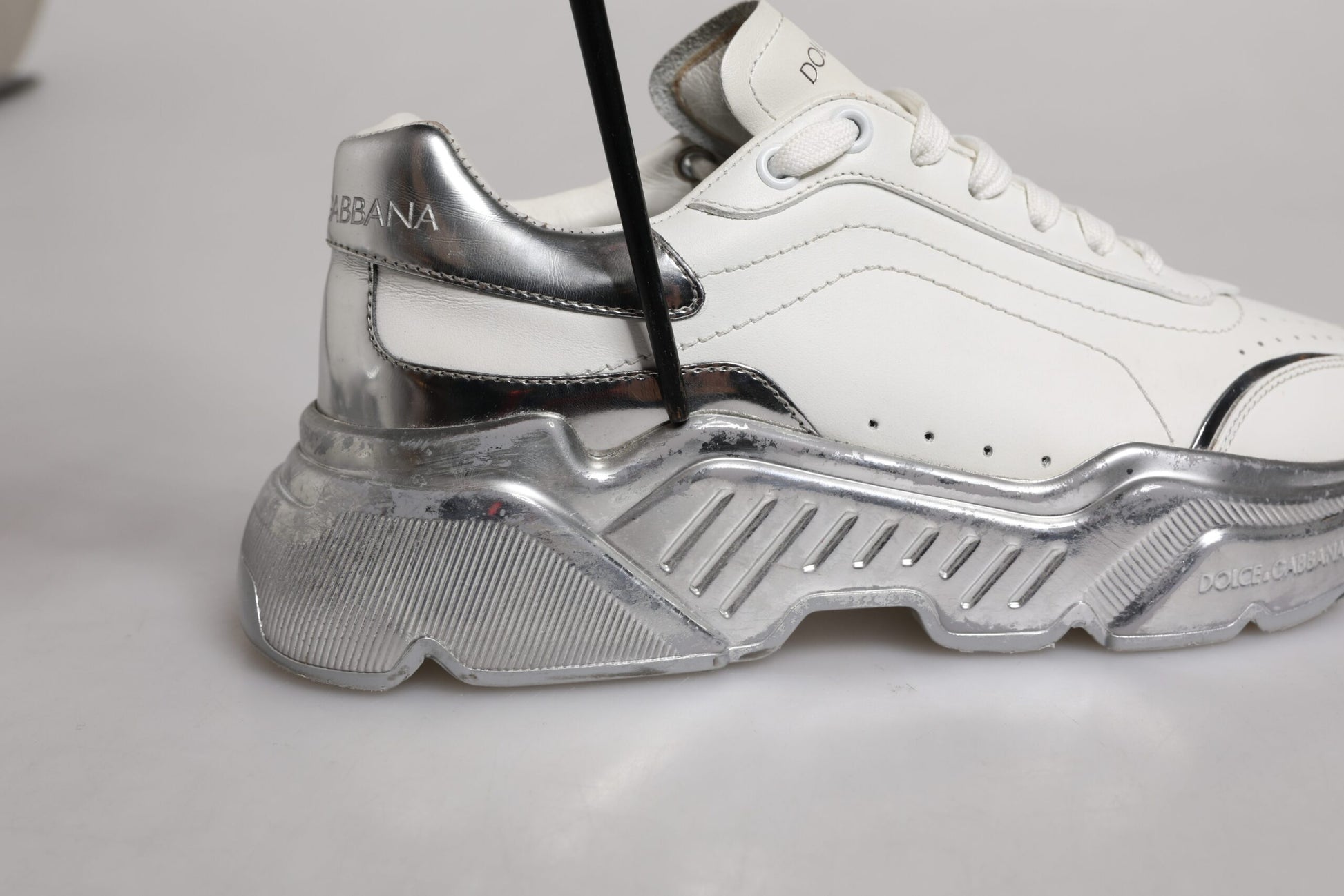 A pair of white and silver sneakers with a low top, featuring the brand name "Dolce & Gabbana" on the side